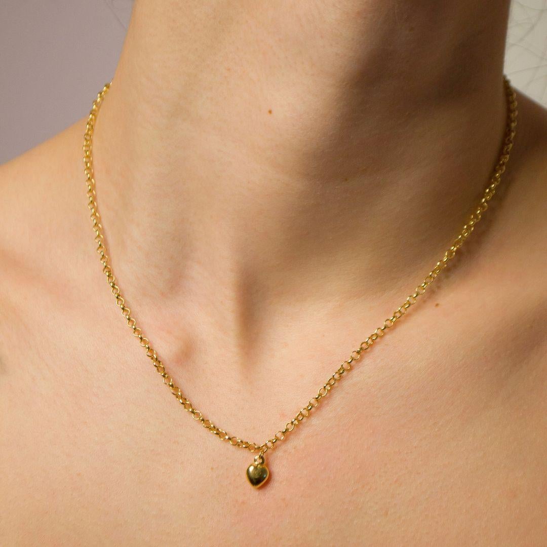 Questa collana a catena rolo in oro giallo 18 carati, realizzata a mano, presenta un delicato ciondolo a forma di cuore, creando una splendida miscela di eleganza senza tempo e fascino moderno. Progettata per essere leggera e confortevole, la