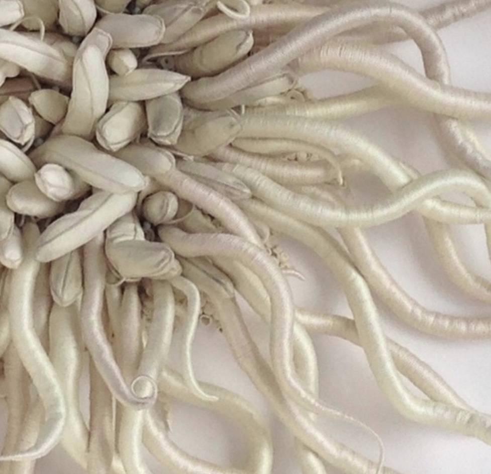 Framed in a pristine acrylic shadowbox Catherine Latson's Specimen 6 reads as an artistic rendition of a beautiful sea specimen. Off-white, oatmeal, and nude hand-dyed thread are wrapped around curly tendrils that condense around an intricate bed of