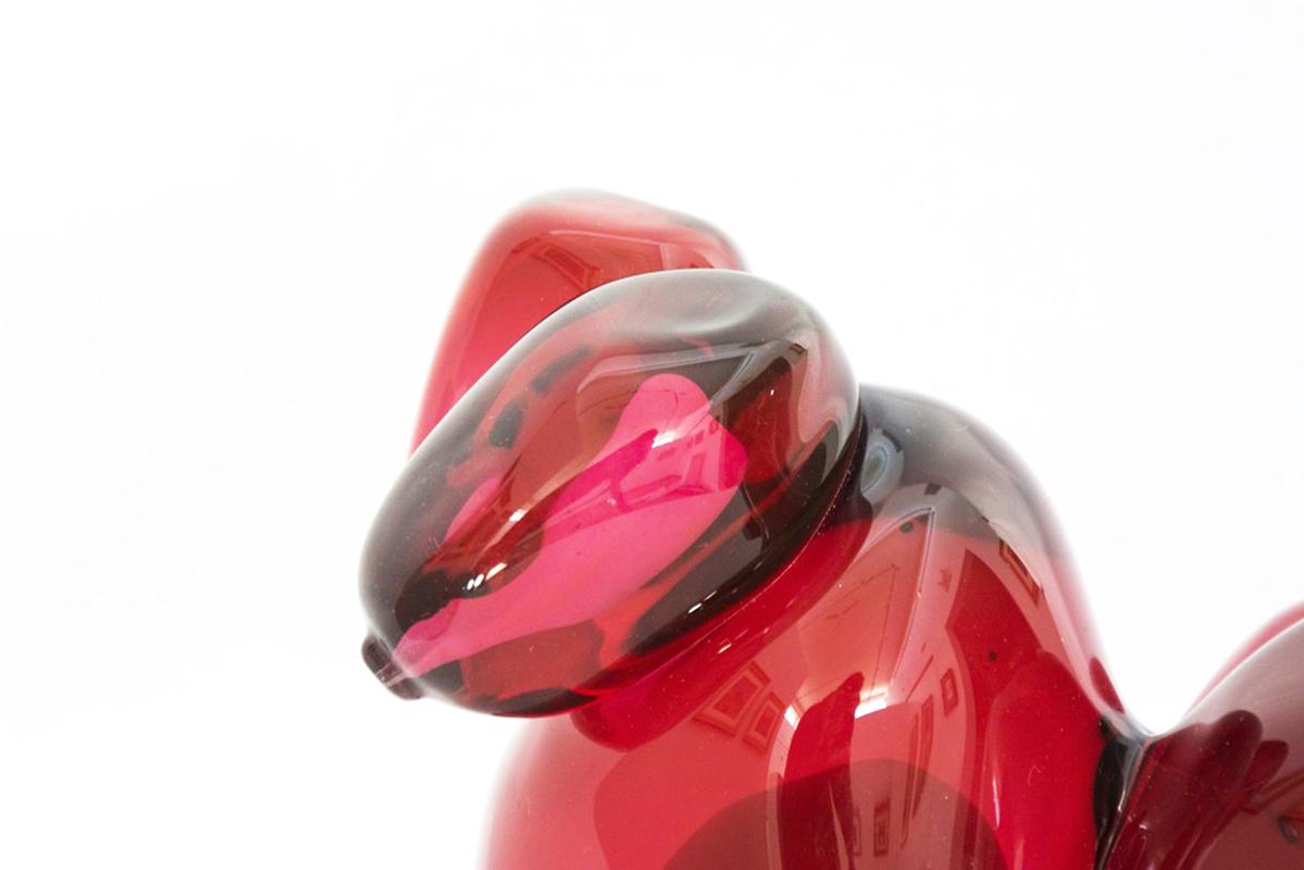 Des formes oblongues groupées et sensuelles en verre rouge translucide ont une surface lisse et polie comme le fruit qui entoure les graines de grenade. Une seule graine se trouve à côté de la grappe. La grenade représente l'abondance, la fortune et