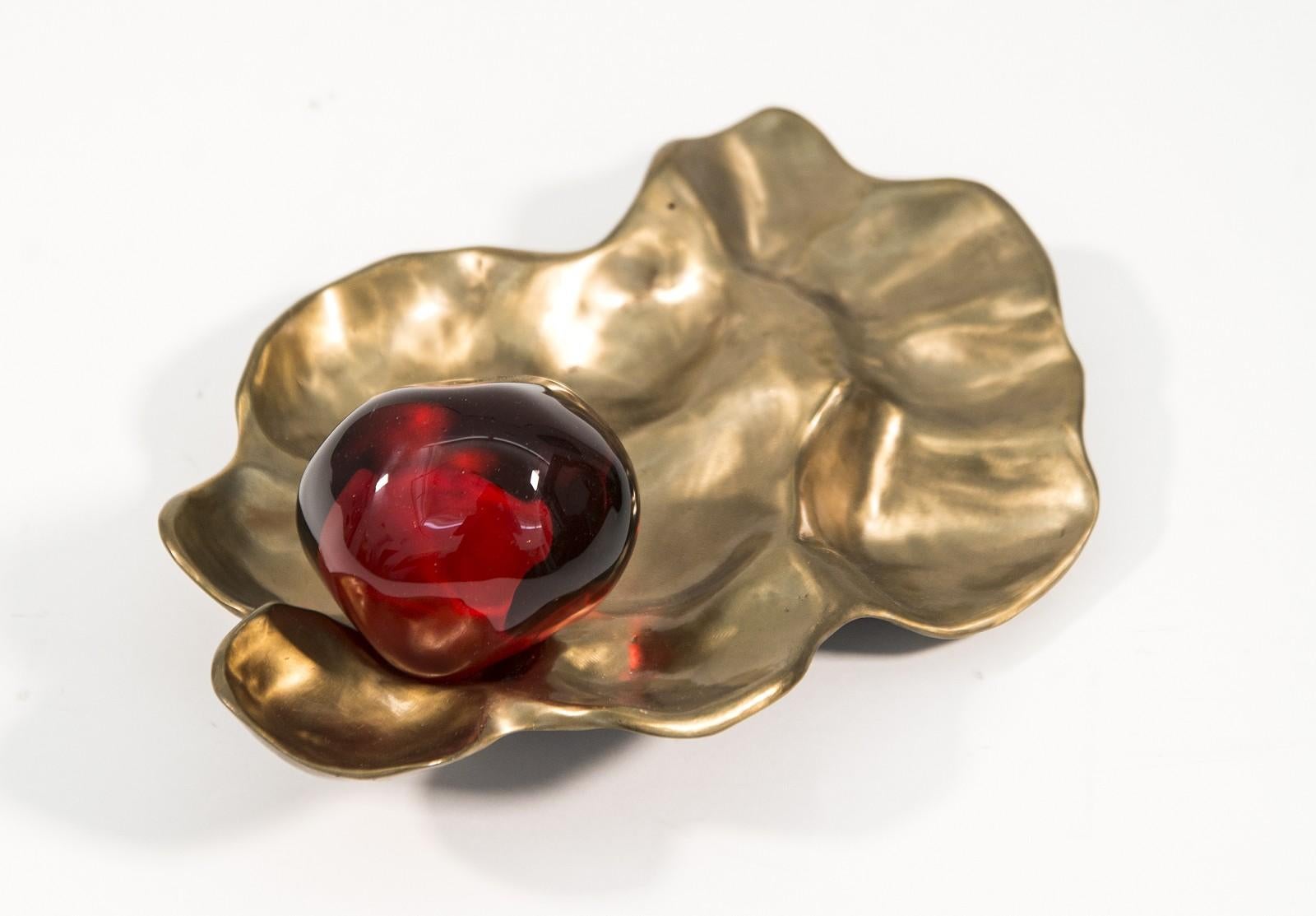 Le verre rouge grenade est niché dans un boîtier en bronze. Vamvakas Lay utilise le bronze et le verre pour créer l'illusion de graines de grenade éparpillées.

Vamvakas Lay incorpore souvent l'imagerie de la grenade combinée au bronze, pour