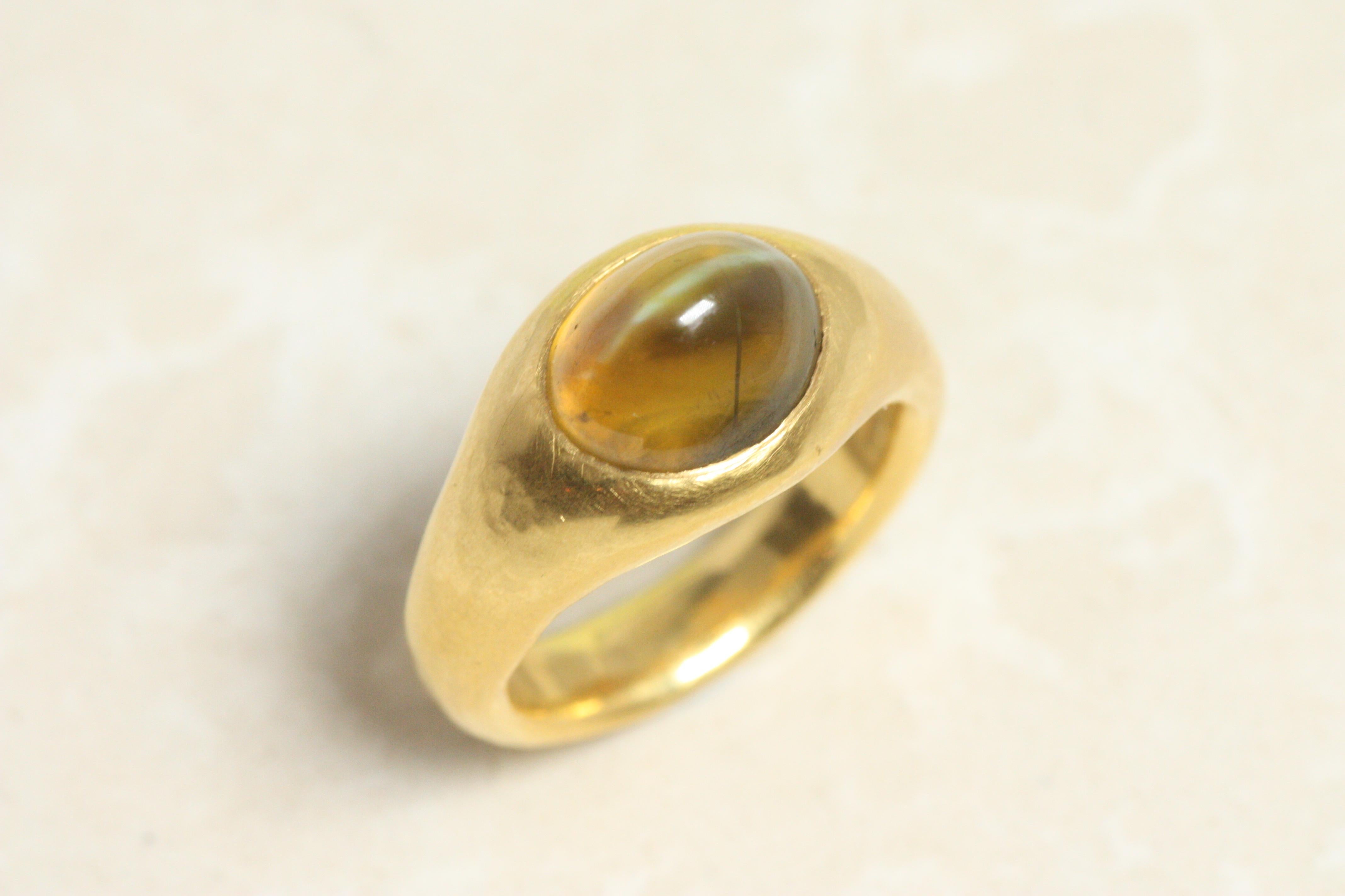 A striking blend of nature’s magic and bold design, this Sri Lankan cat’s-eye gemstone (6.82ct) displays a mesmerizing chatoyancy—a silky, glowing line that moves across its honey-green depths. Set in a substantial 22K gold gypsy-style band, this