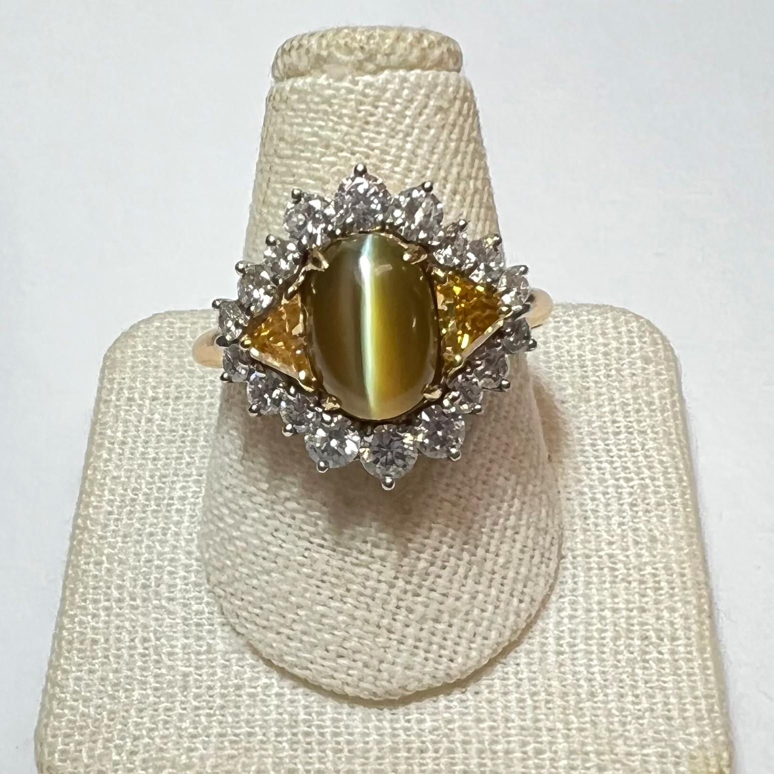 Fine cat's eye chrysoberyl weighing an estimated 7.00ct, set in an 18kt yellow gold mounting.  Flanked by two triangular fancy yellow diamonds totaling approximately 0.66ct. Surrounded by eighteen round brilliant cut diamonds totaling 1.16ct.  The