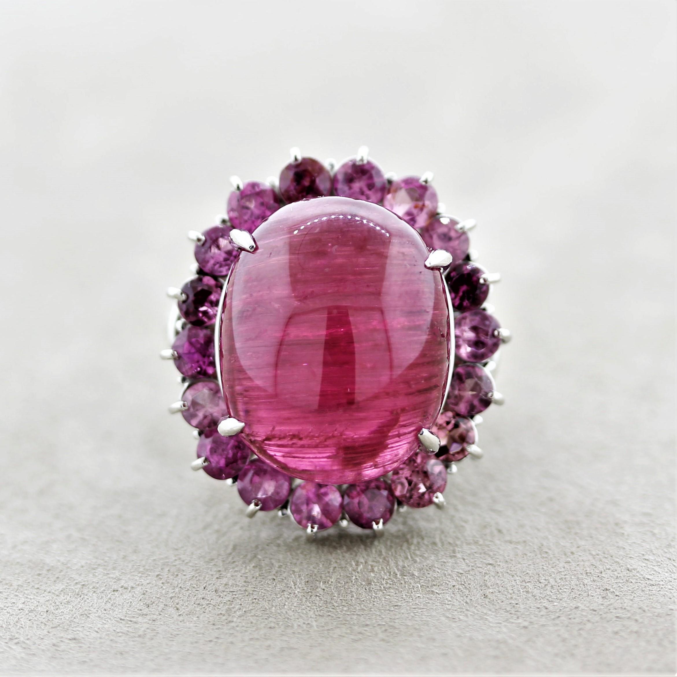 A large and impressive cocktail ring featuring a 27.25 carat cats eye tourmaline. It has a rich royal red color making it a Rubellite in the trade. It is haloed by additional tourmalines, pink tourmalines, weighing 4.18 carats. Adding to that are