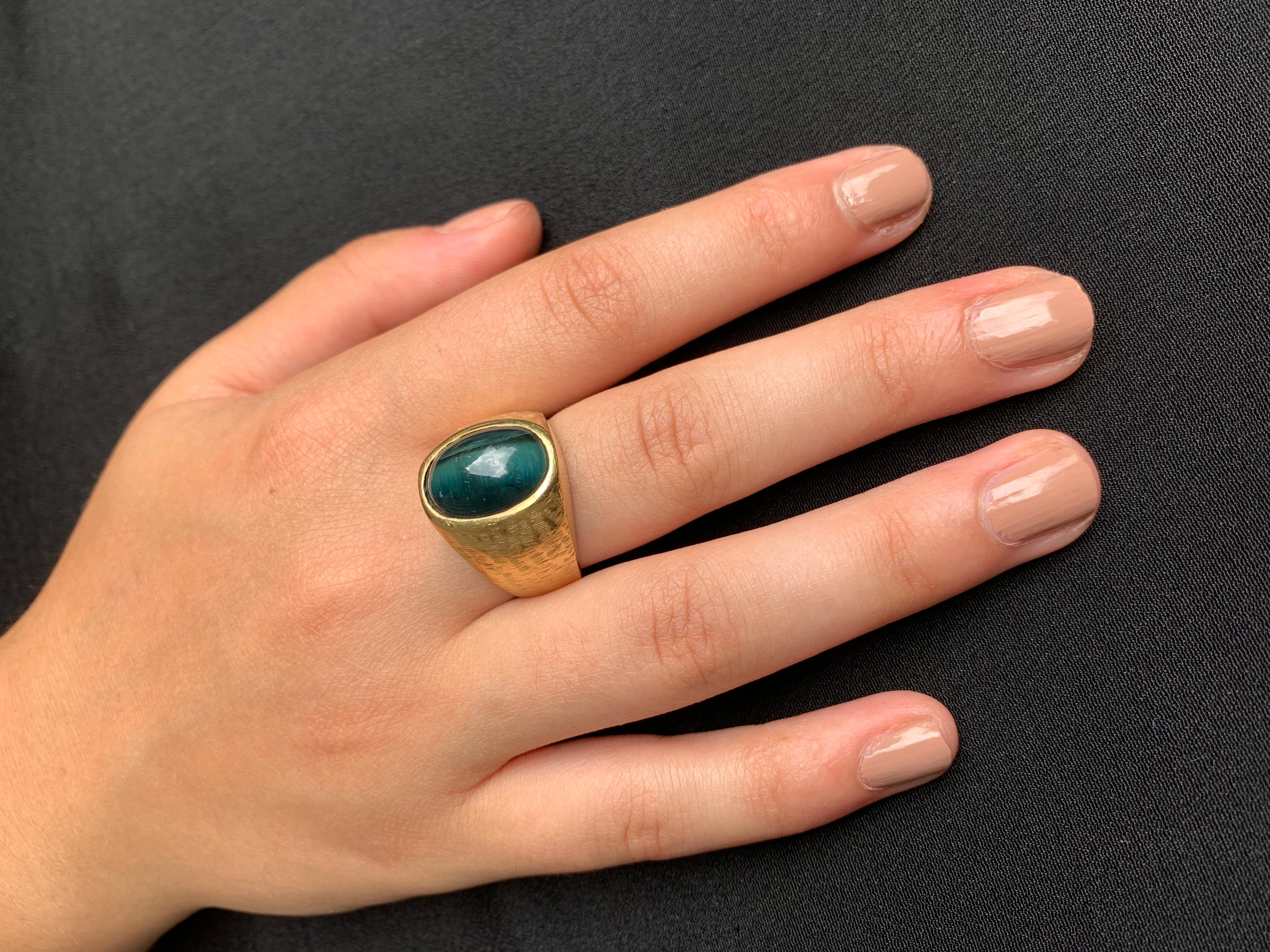Classic, elegant ring. Substantial cabochon cat's eye tourmaline measuring 15mm by 11mm with a well defined chatoyancy effect, color range green with blueish undertone, set in a textured 18K yellow gold setting, marked 750 on the interior of band