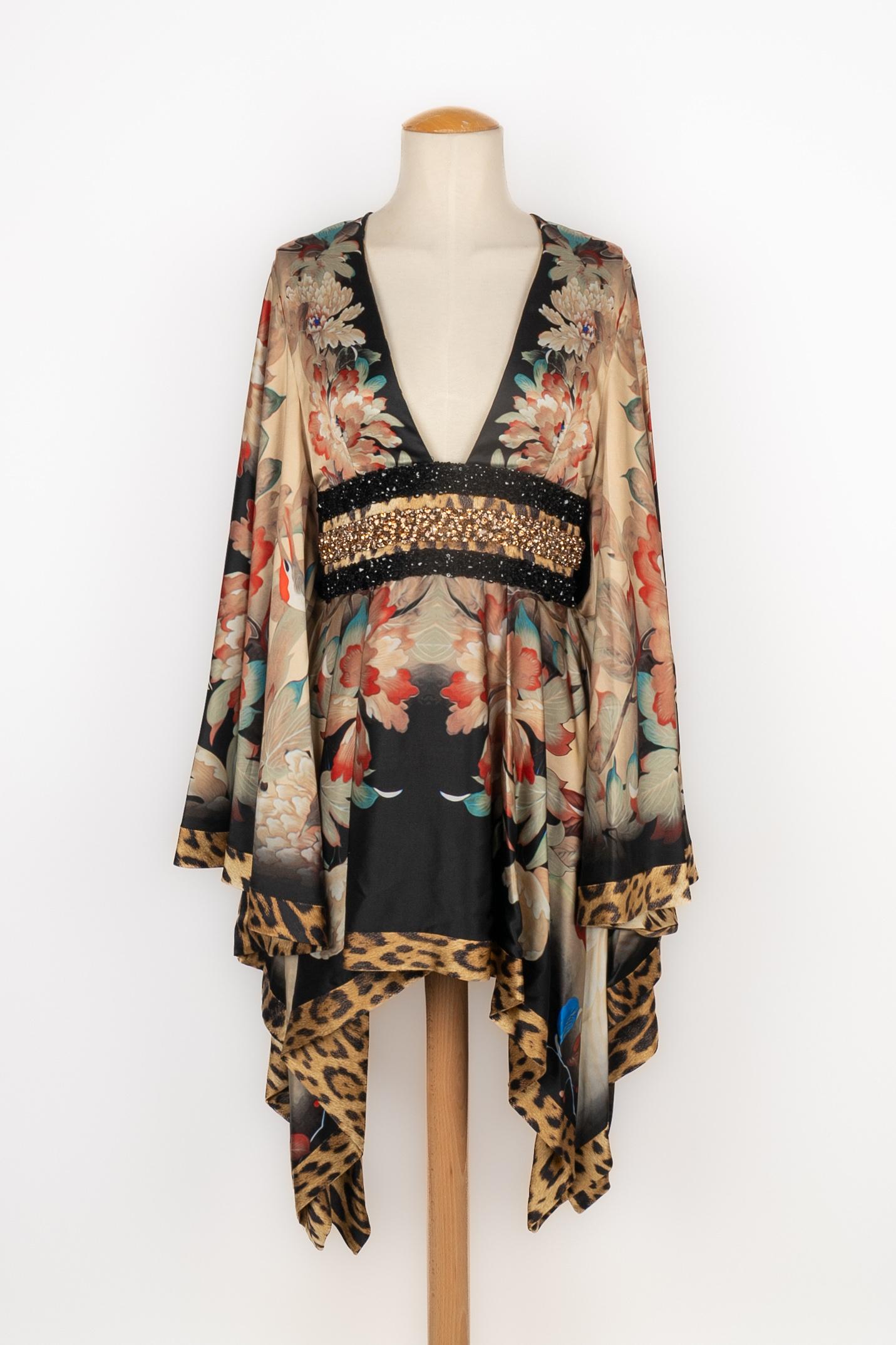 CAVALLI - Minikleid aus Seide, bedruckt mit rosa und blauen Blumen und mit einem Saum mit Geparden-Print. Der Bund ist mit goldenen Perlen und schwarzen Pailletten verziert. Ärmel im Fledermausschnitt. Größe 42IT.

Bedingung:
Sehr guter