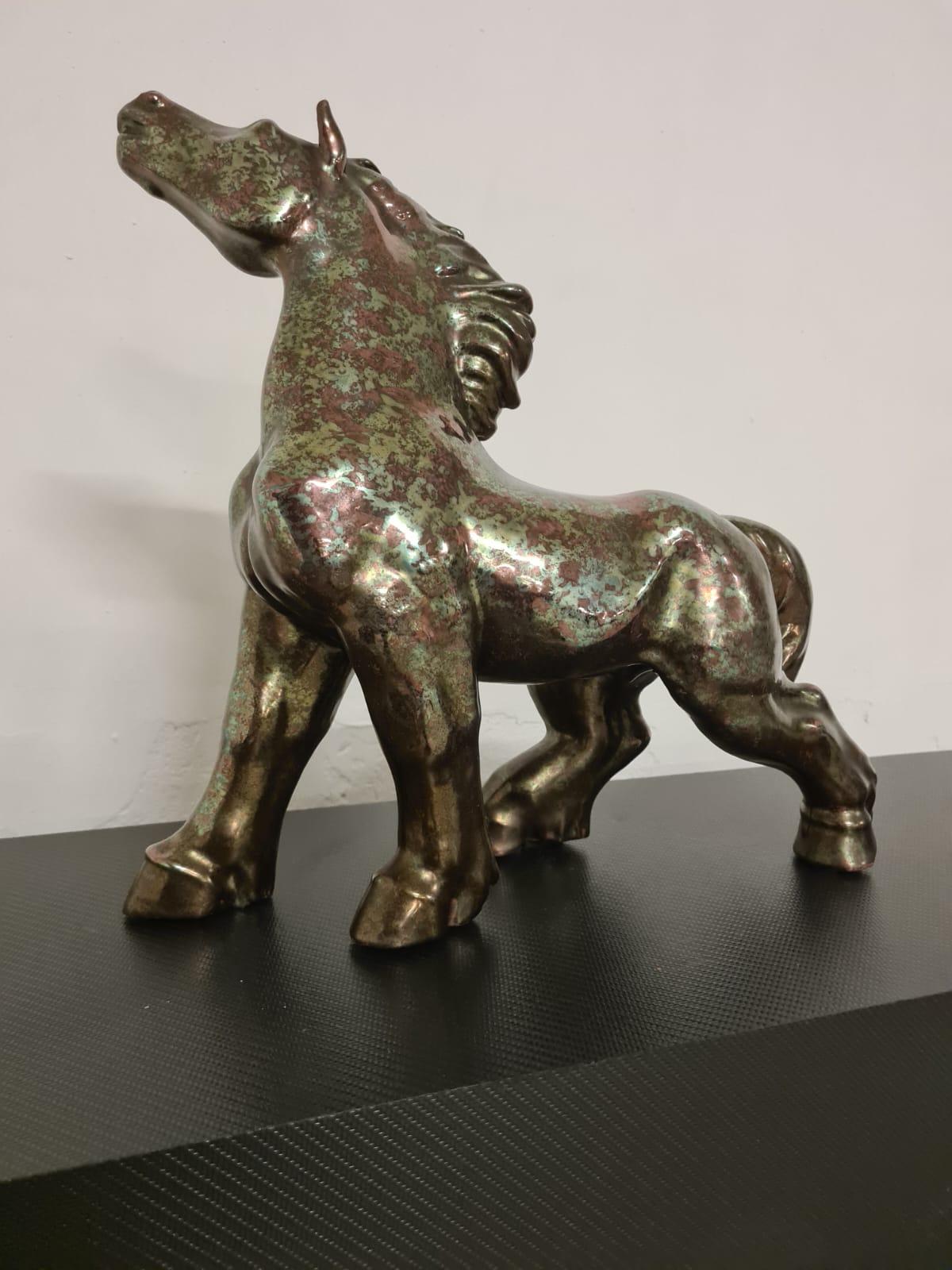 Poderoso caballo de cerámica esmaltada de albissola.

Elegante caballo de cerámica esmaltada con colores marrón y verde que aumentan su potencia y le dan un efecto bronce.

El caballo es sorprendido en el acto de mover la cabeza.

En términos de