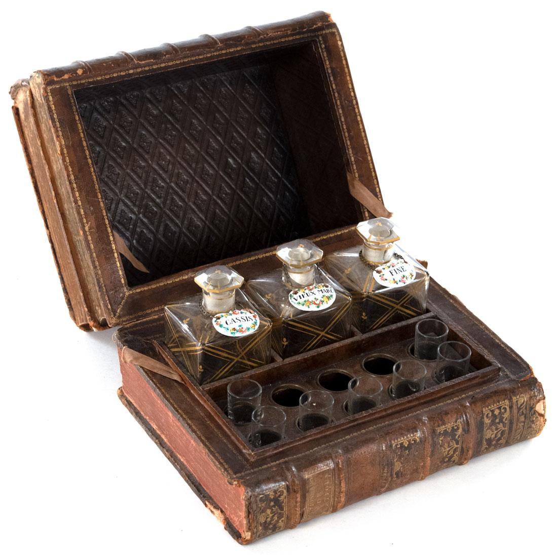 Disguised as three leather-bound French novels, this liquor cabinet opens to reveal a stamped and gilt leather interior with seven custom drinking glasses and three gilt and blown glass liquor bottles with stoppers and porcelain labels.
