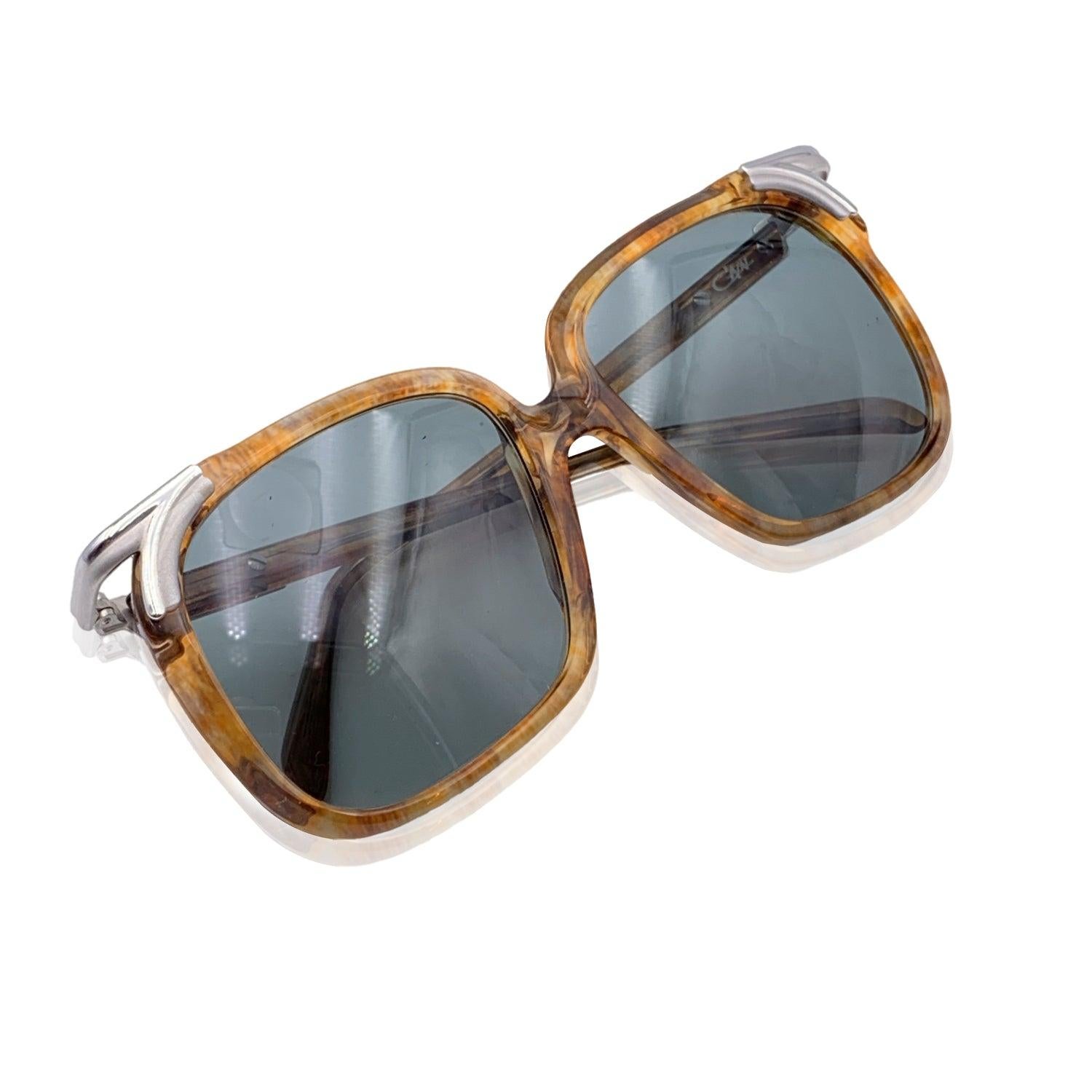Entra nel mondo del lusso audace e vintage con questi occhiali da sole Cazal, modello 112 col. 69. Questi occhiali da sole sono caratterizzati da una montatura marrone semi-chiara che cattura l'essenza dello stile degli occhiali degli anni '80:
