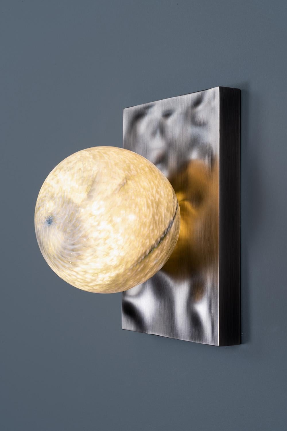 Cloudbreak: 201 Sconce was inspired by the shells and other sea life left behind in the wave patterned sand of receding tides. Like little pearls nestled in oysters, our hand blown glass sits perfectly on a wave patterned, CNC milled brass back