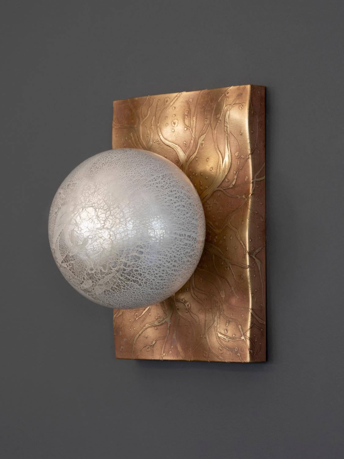 Cloudbreak: 201 Sconce was inspired by the shells and other sea life left behind in the wave patterned sand of receding tides. Like little pearls nestled in oysters, our hand blown glass sits perfectly on a wave patterned, CNC milled brass back