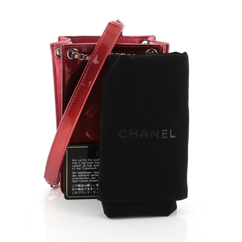 This Chanel CC Phone Holder Crossbody Bag Patent, crafted in red patent leather, features woven-in leather chain strap with leather pad, front stitched CC detail, expandable sides, and gunmetal-tone hardware. It opens to a black fabric interior.