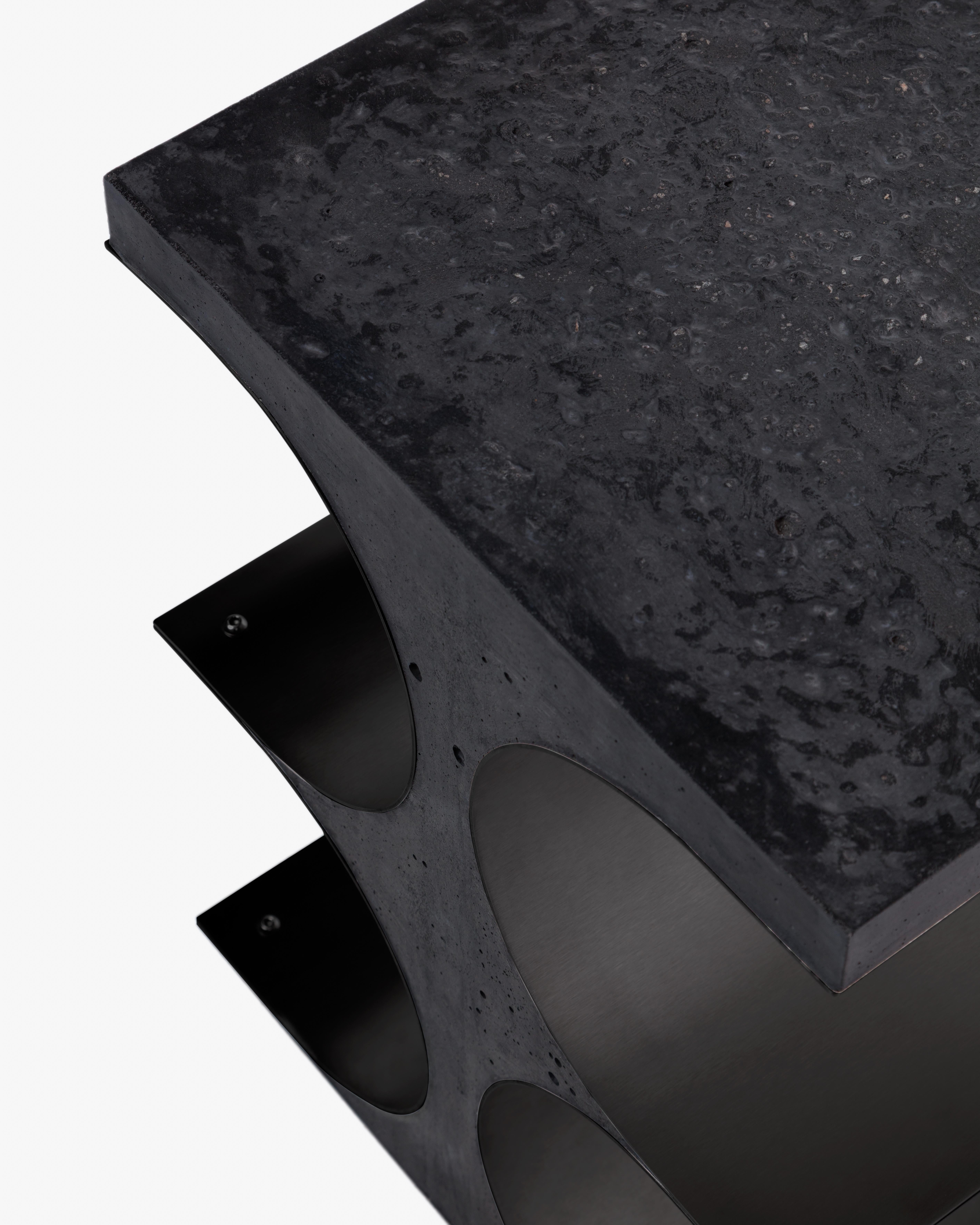 This side table in black concrete emphasizes architectural weight, while the void between curved steel panels creates a rhythm of mass and absence. Sculptural yet functional, it reflects Simões’ formal precision and his use of material tension to