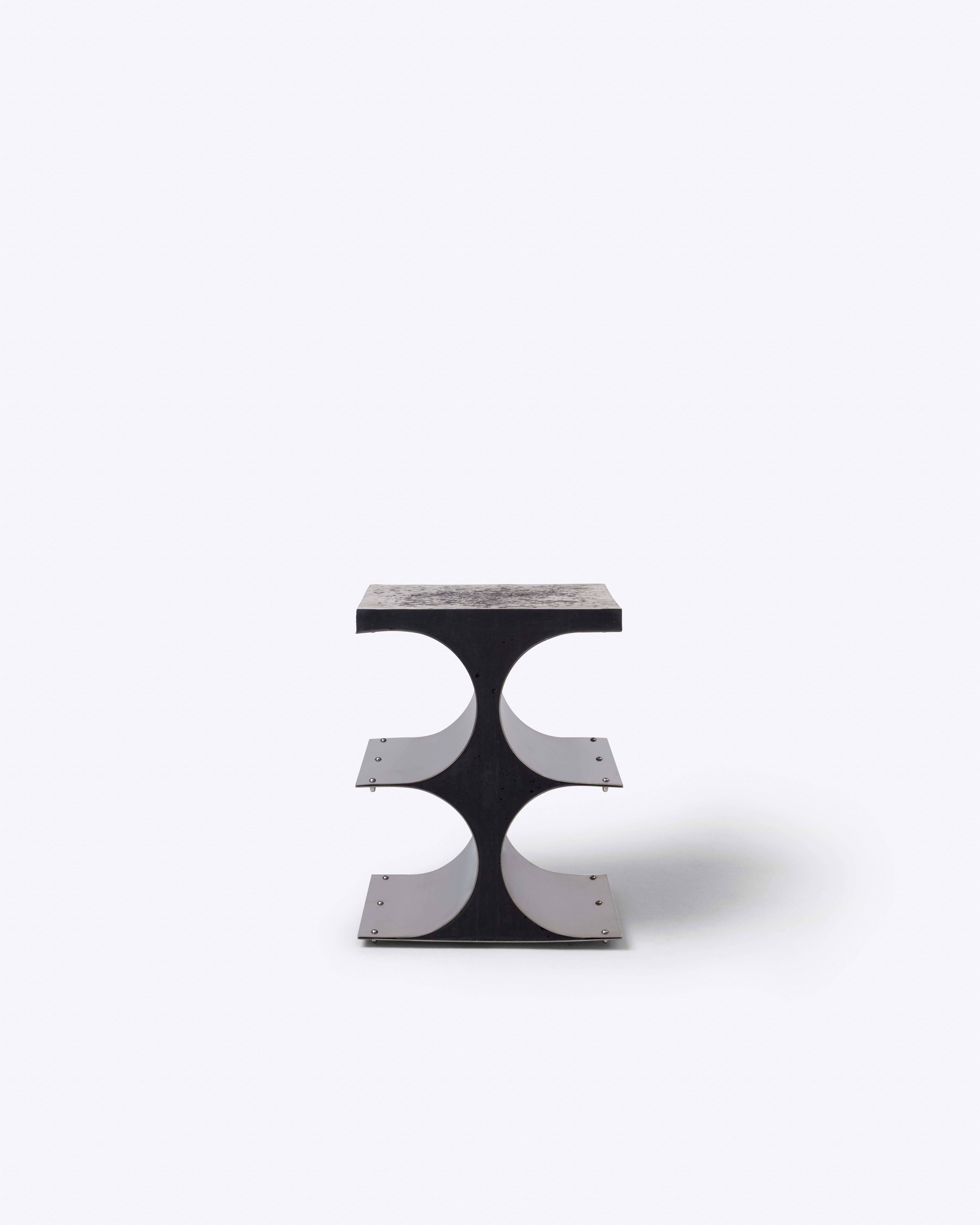 This iteration pairs black concrete with brushed stainless steel, heightening contrast and architectural rigor. The void between curved panels introduces a sculptural rhythm, while the piece remains functional yet formally assertive— showcasing