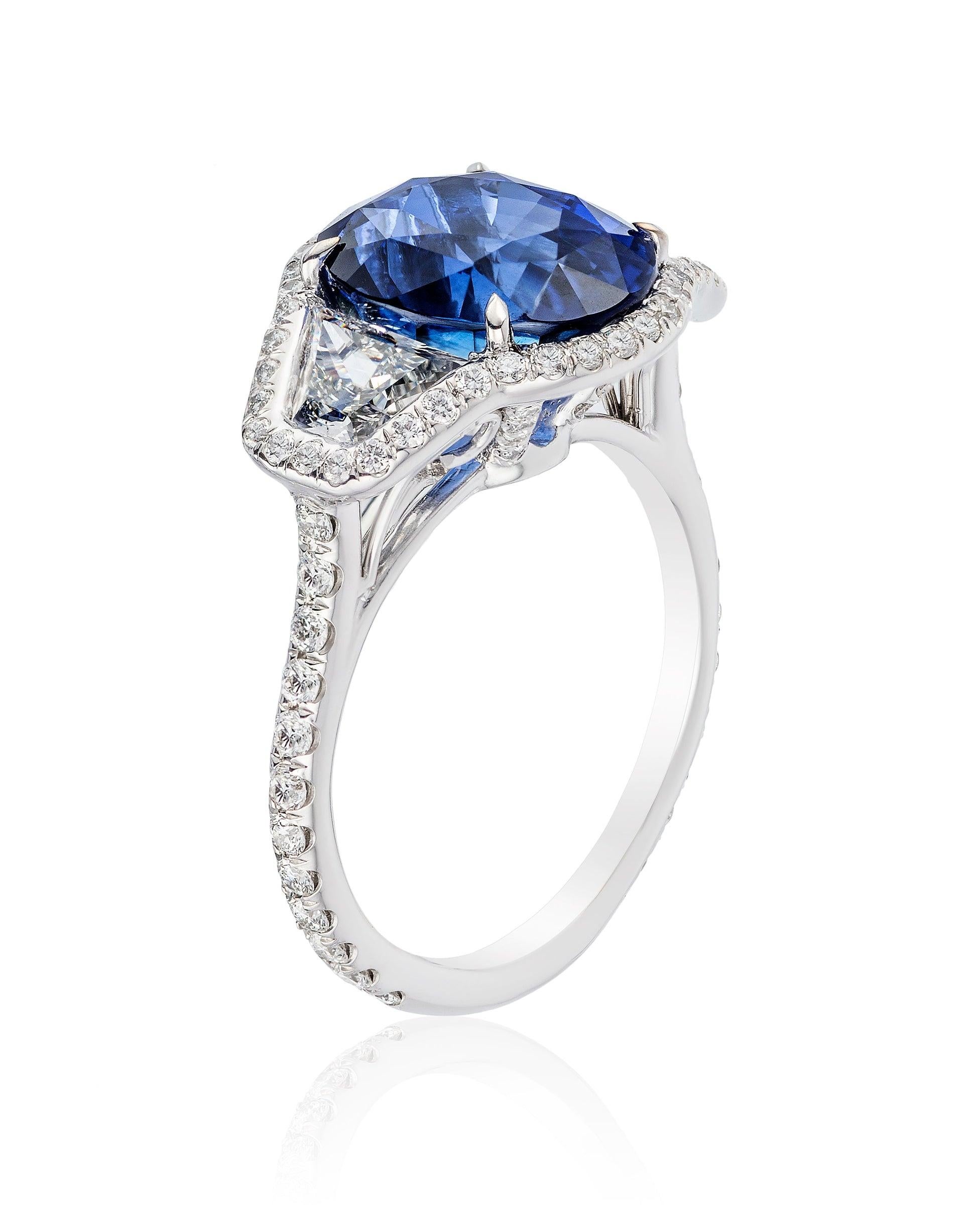 A platinum ring featuring a large Blue Sapphire accompanied by two diamonds (1.12 carats total), beautifully adjoined by a halo and band that together feature 64 sparkling micro-diamonds.
 
Details
Center: Blue Sapphire – 6.22ct
Dimensions : 11.36 x