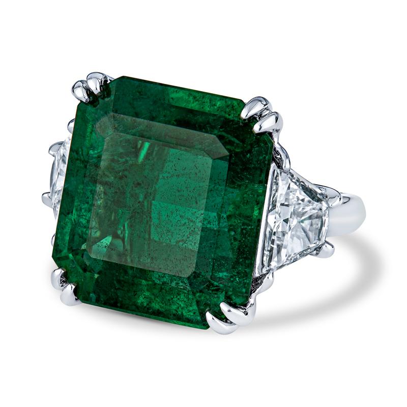 This is a one of a kind cocktail ring featuring a stunning 15.71 carat vivid green natural Zambian octagonal step cut emerald. It is accented by two trapezoid diamonds weighing 1.63 carat total weight, G VS2, and is set in platinum. The ring is a
