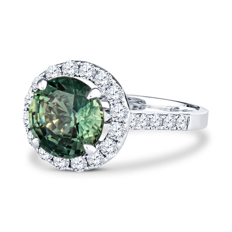 This beautiful ring features a 3.38 carat round cut natural green sapphire accented with 0.75 carat total weight in round brilliant cut diamonds set in 18 karat white gold. It is a size 7 but can be resized upon request. 
Measurements: 8.99-9.11 x