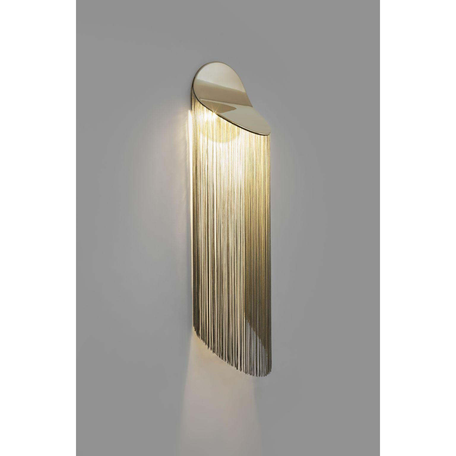 Cé wall lamp by Studio d'Armes
Design by Alexandre Joncas
Dimensions: 25 x 20 x H 100 cm
Materials:  12k Gold Plated Steel, Rayon fringes offered in different colors 
 
Design by Alexandre Joncas
Cé jostles the obvious association between fringes