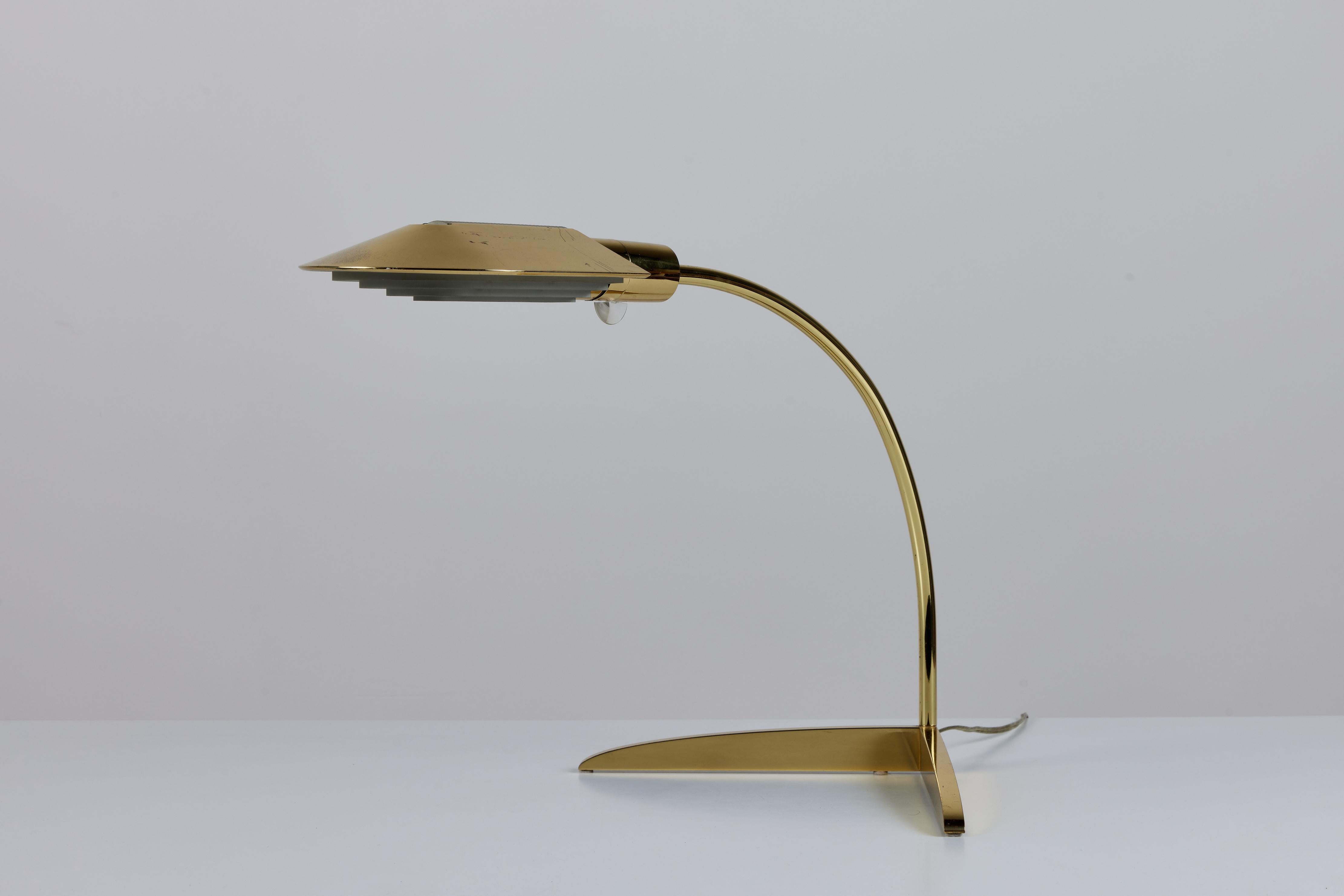 Designed in the 1970s, the brass desk lamp by Cedric Hartman is an enduring design classic. The modernist lamp features a domed oval brass shade attached to a curved stem that offers focused task lighting. The arched brass pole terminates into a