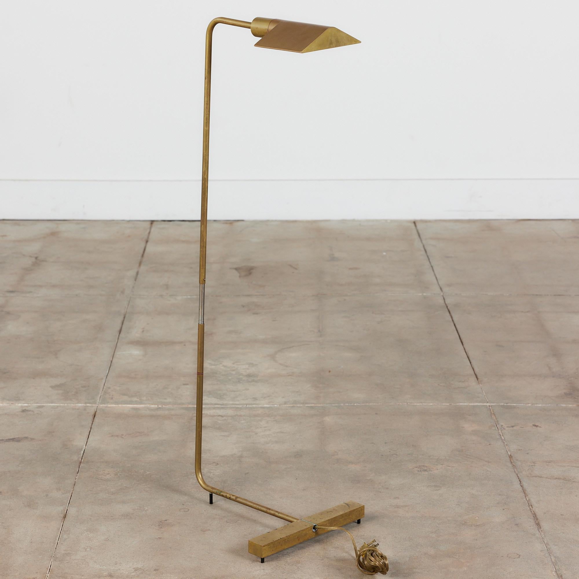 Designed in the 1970s, this brass floor lamp by Cedric Hartman is an enduring design classic. The modernist floor lamp features a triangular brass shade attached to a curved stem that offer focused task lighting. The arched brass pole terminate into
