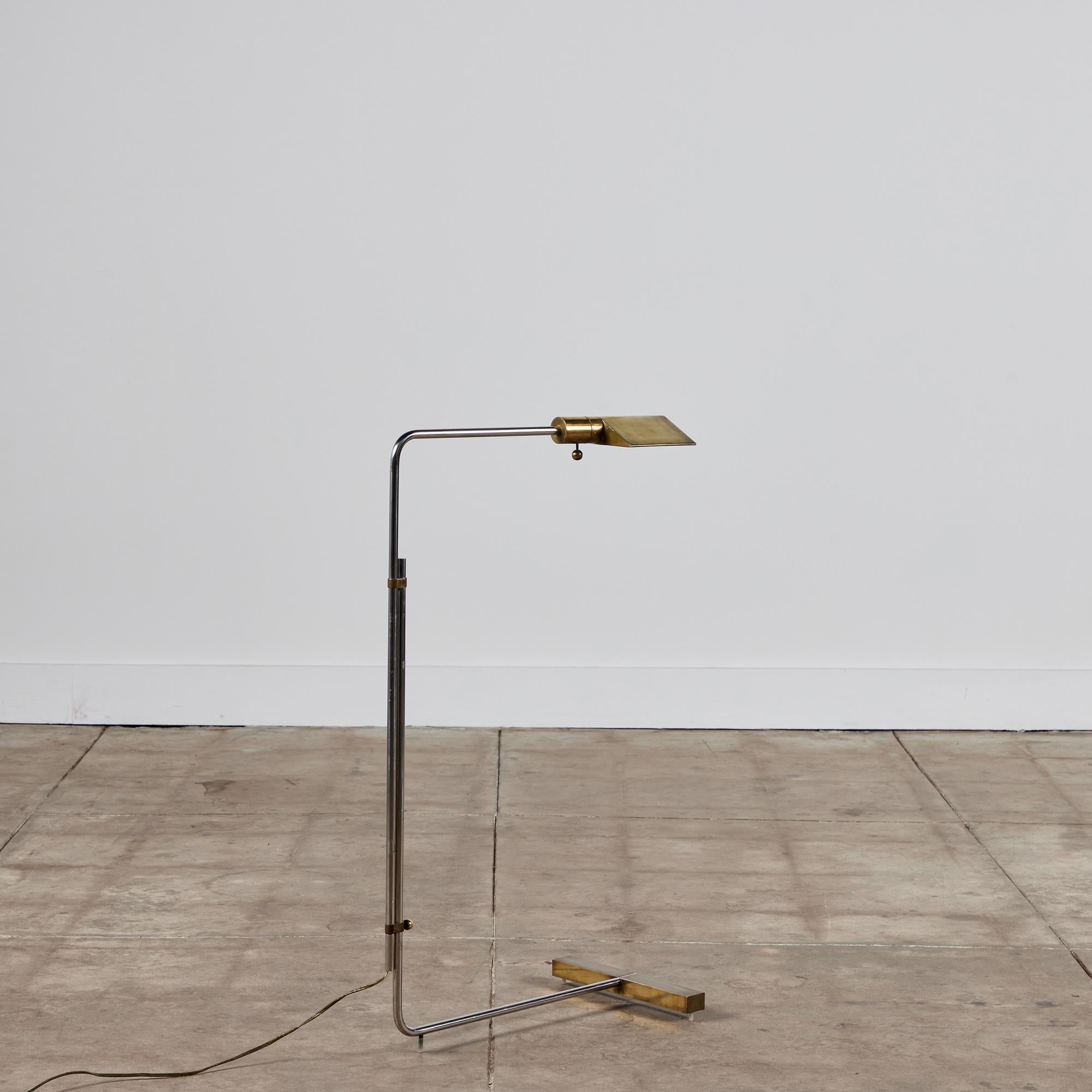 Designed in the 1970s, this brass and stainless steel floor lamp by Cedric Hartman is an enduring design Classic. The modernist floor lamp features a triangular brass shade attached to two curved parallel stainless steel stems that offer focused
