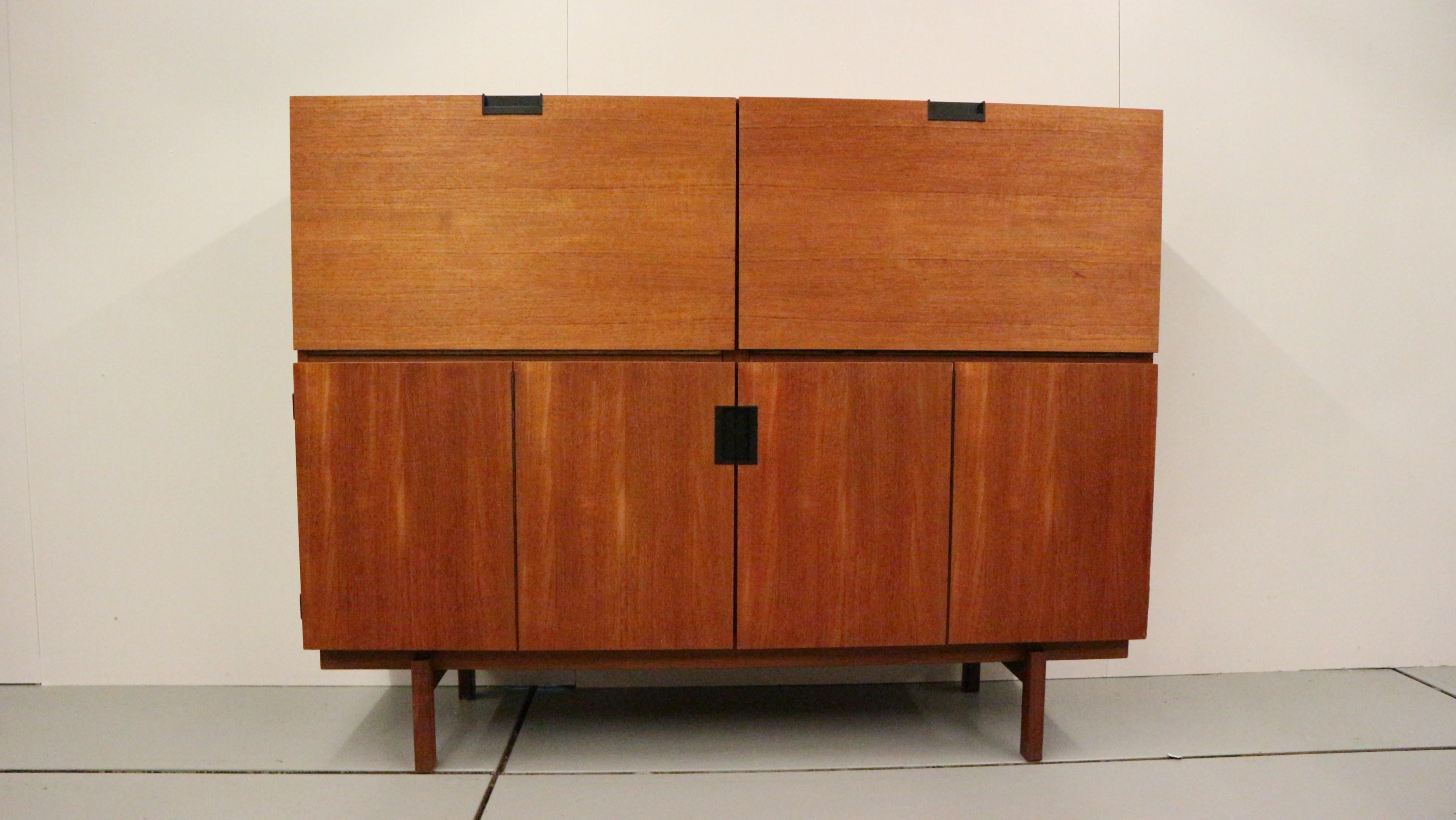 This is for a Minimalist model CU05 cabinet designed by Cees Braakman and manufactured by Pastoe UMS, The Netherlands 1958. This highboard is made of teak wood veneer and has a solid wooden frame. The handles are made of black plastic.  Two folding