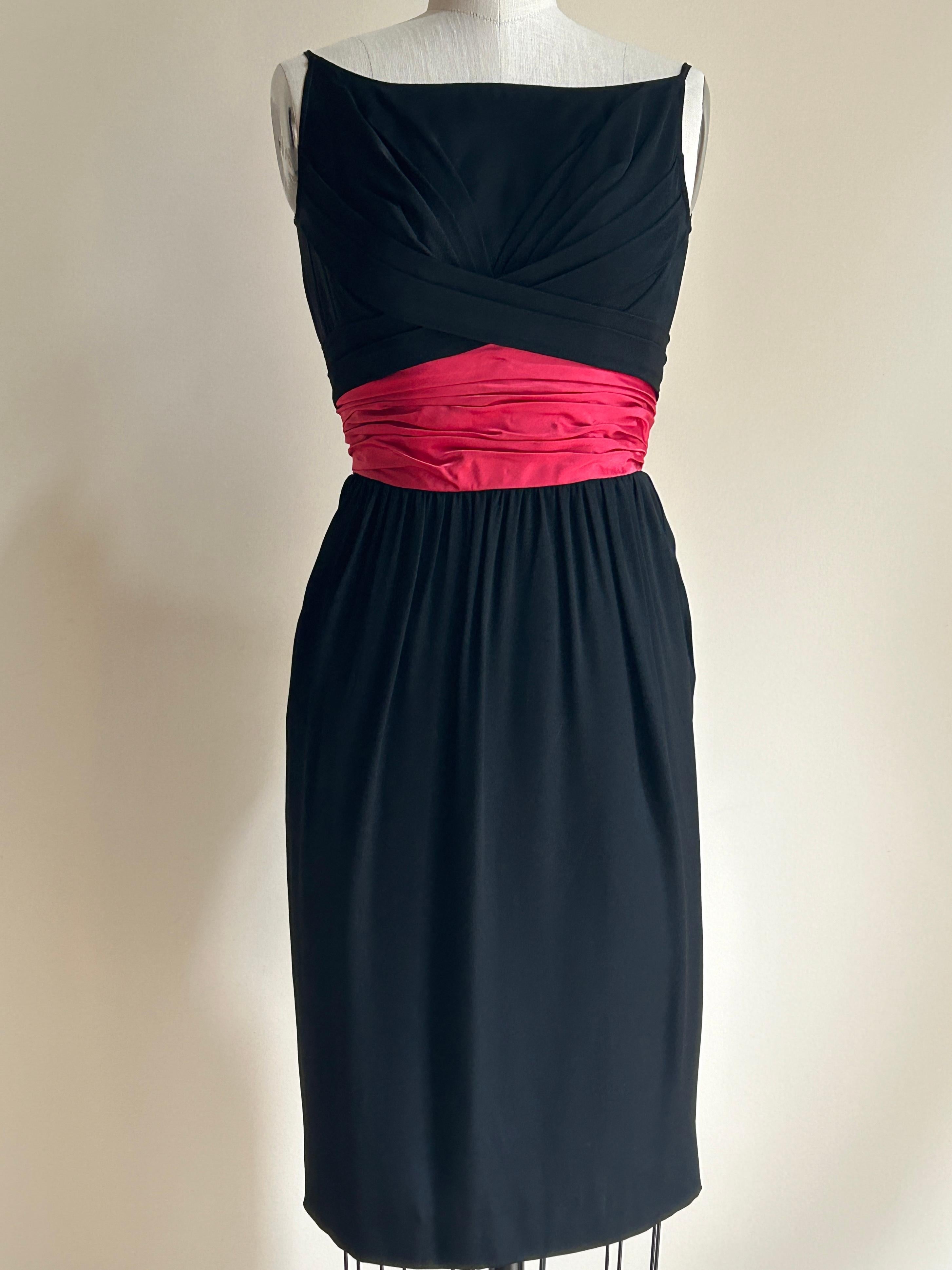 Ceil Chapman vintage 1950s sleeveless black boatneck dress with skinny straps at top shoulder and crossed pleat detail at front and back bodice. Skirt is gathered at deep pink/red attached satin sash-like detail at waist. Back zip (there are hook