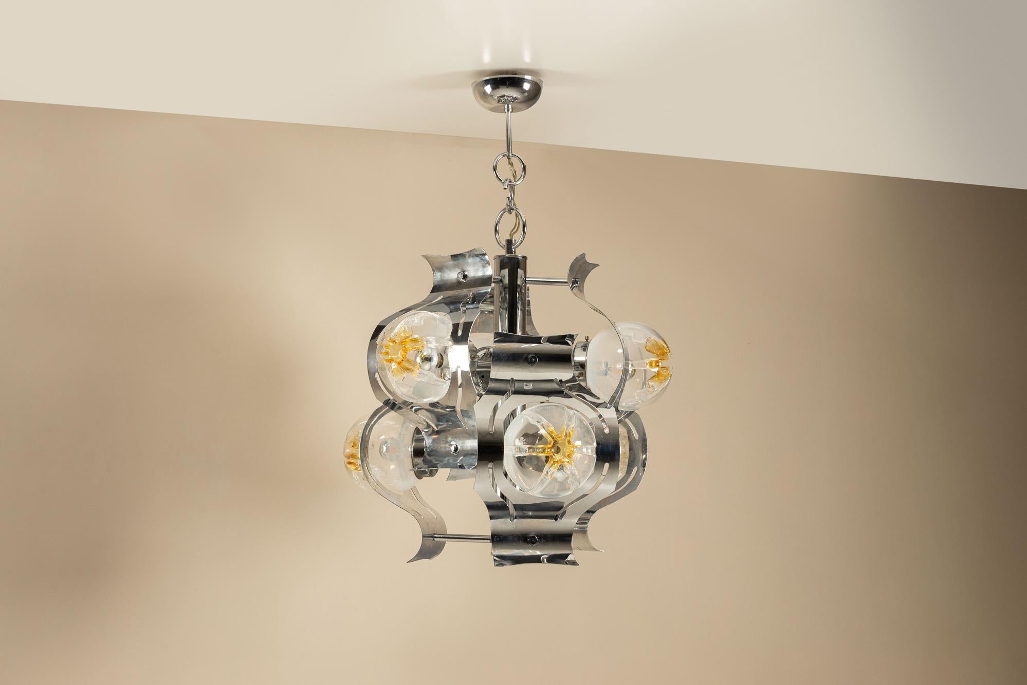 Una composizione luminosa di Mazzega in cromo e vetro di Murano. Questo lampadario di Mazzega, progettato all'inizio degli anni '70, cattura l'eleganza e l'energia sperimentale del design italiano dell'illuminazione al suo apice.

Design
La lampada