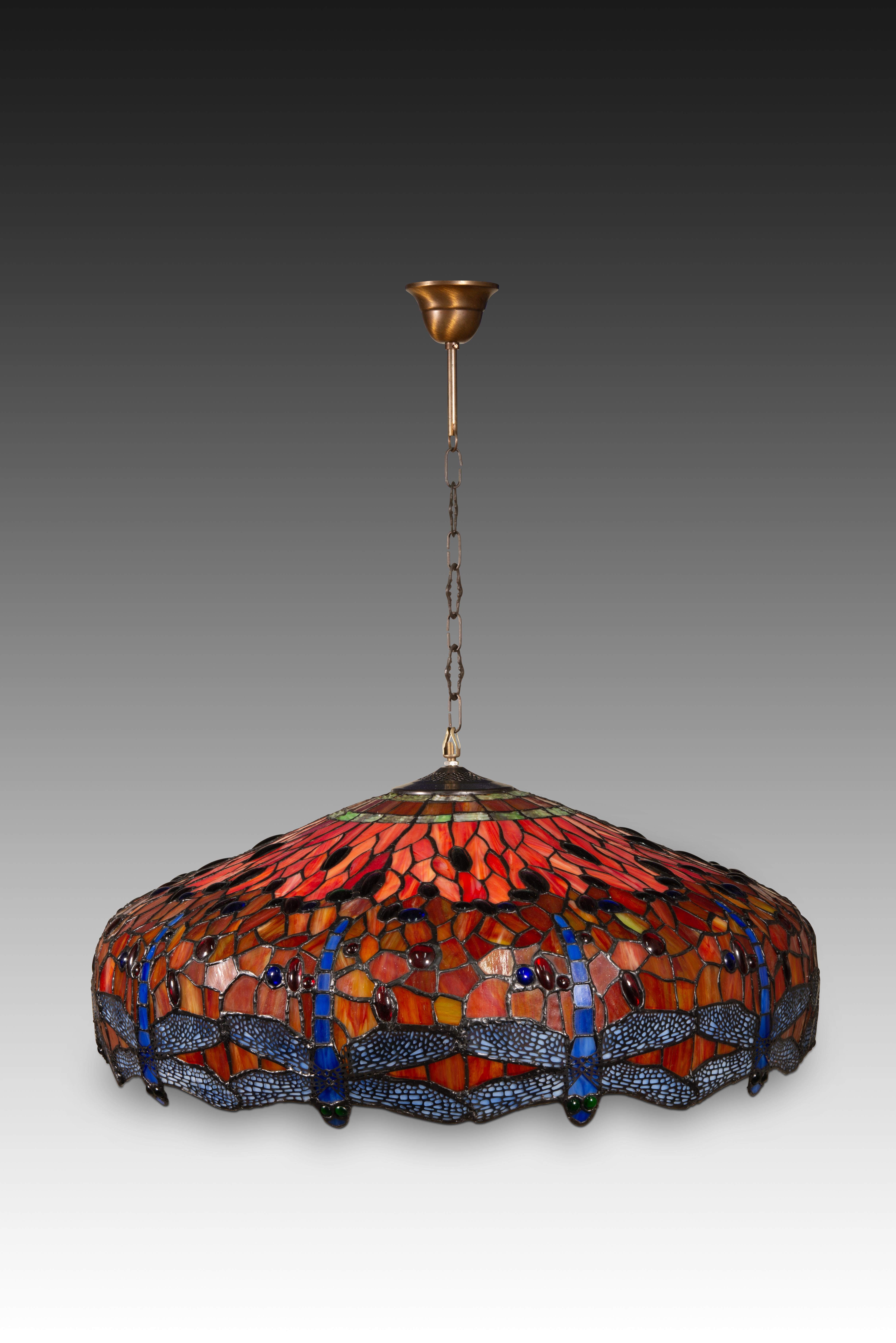  Lampada da soffitto, stile Tyffany. Polimero, metallo. XX secolo. 
Lampada da soffitto con un punto luce, catena per appendere e paralume in polimero di vari colori che ricorda le consuete e apprezzate composizioni di Stained Glass di Tyffany. -