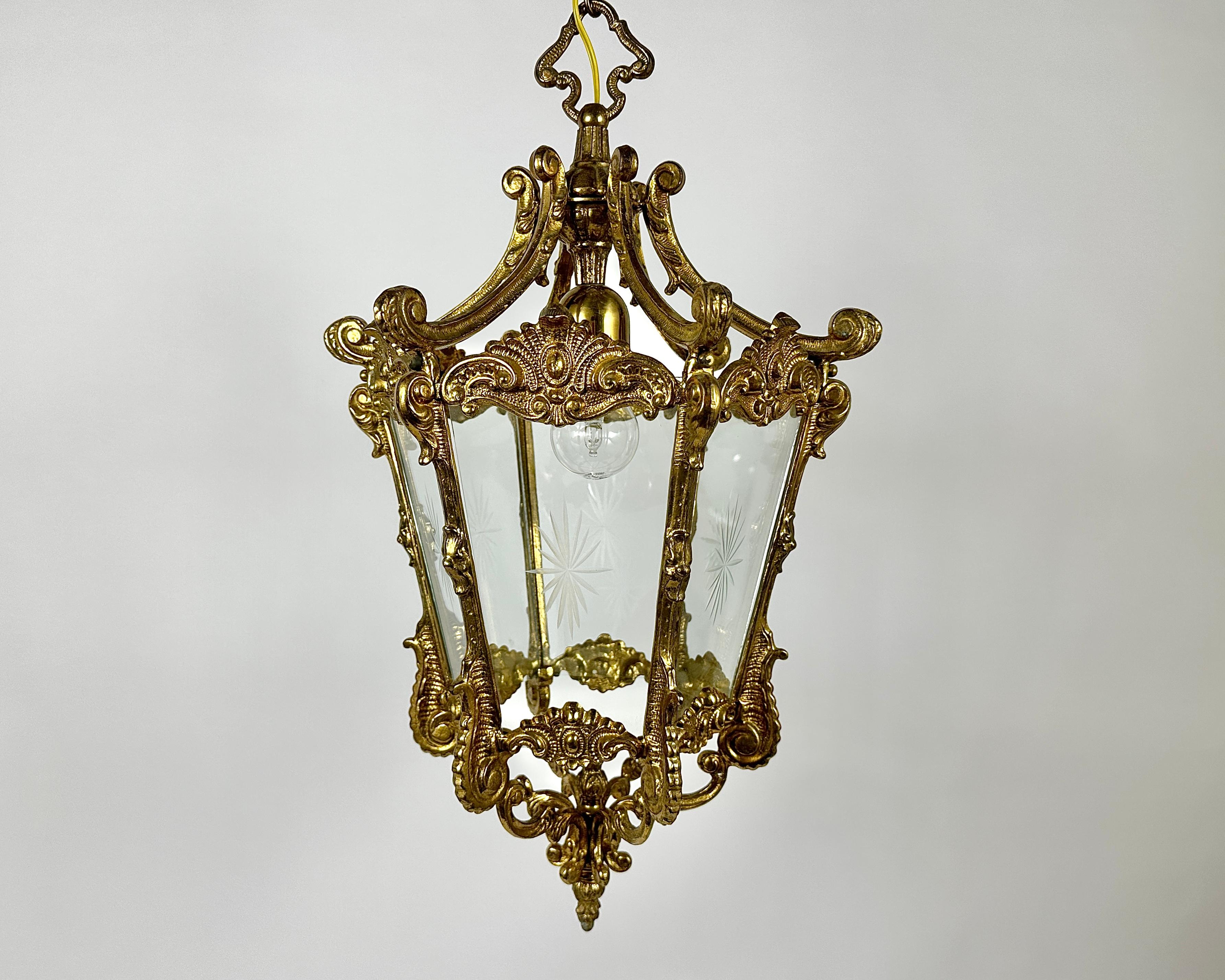 Antique gilded bronze hall lantern with one lamp surrounded by sectional convex tapering glass panels and held within a foliated scrolling framework with decorative central pierced leaves and open scrolling canopy, having the original chain and