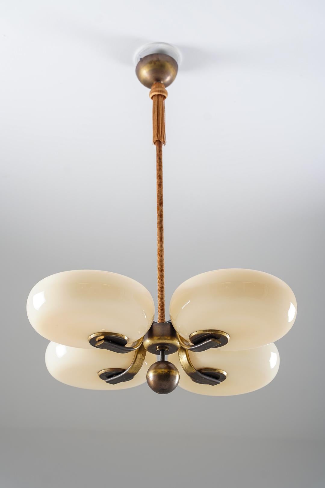 Frühe Deckenleuchte, entworfen von Paavo Tynell für Taito in den 1930er Jahren. Die Leuchte besteht aus vier cremefarbenen Glasschirmen mit sanft gerundeten Formen, die um eine zentrale Messingkugel angeordnet sind. Die geschwungenen Messingarme