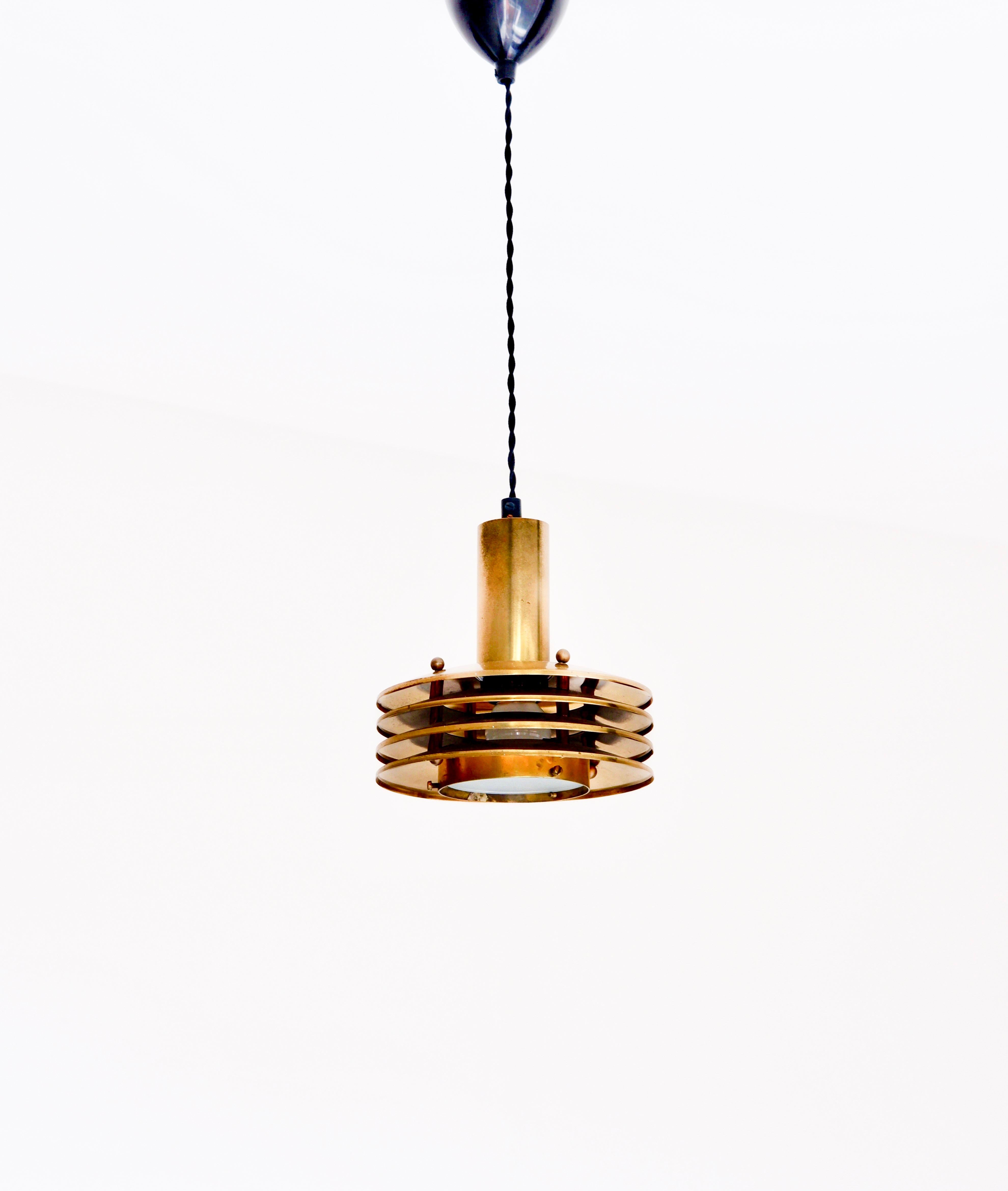 Rare pendant designed by Kai Ruokonen, made in solid brass with 4 rings and a glass diffuser. The overhall condition is good and the lamp has a good patina with trace of use and age. The lamp is composed by 4 lamp shade rings hold them together by