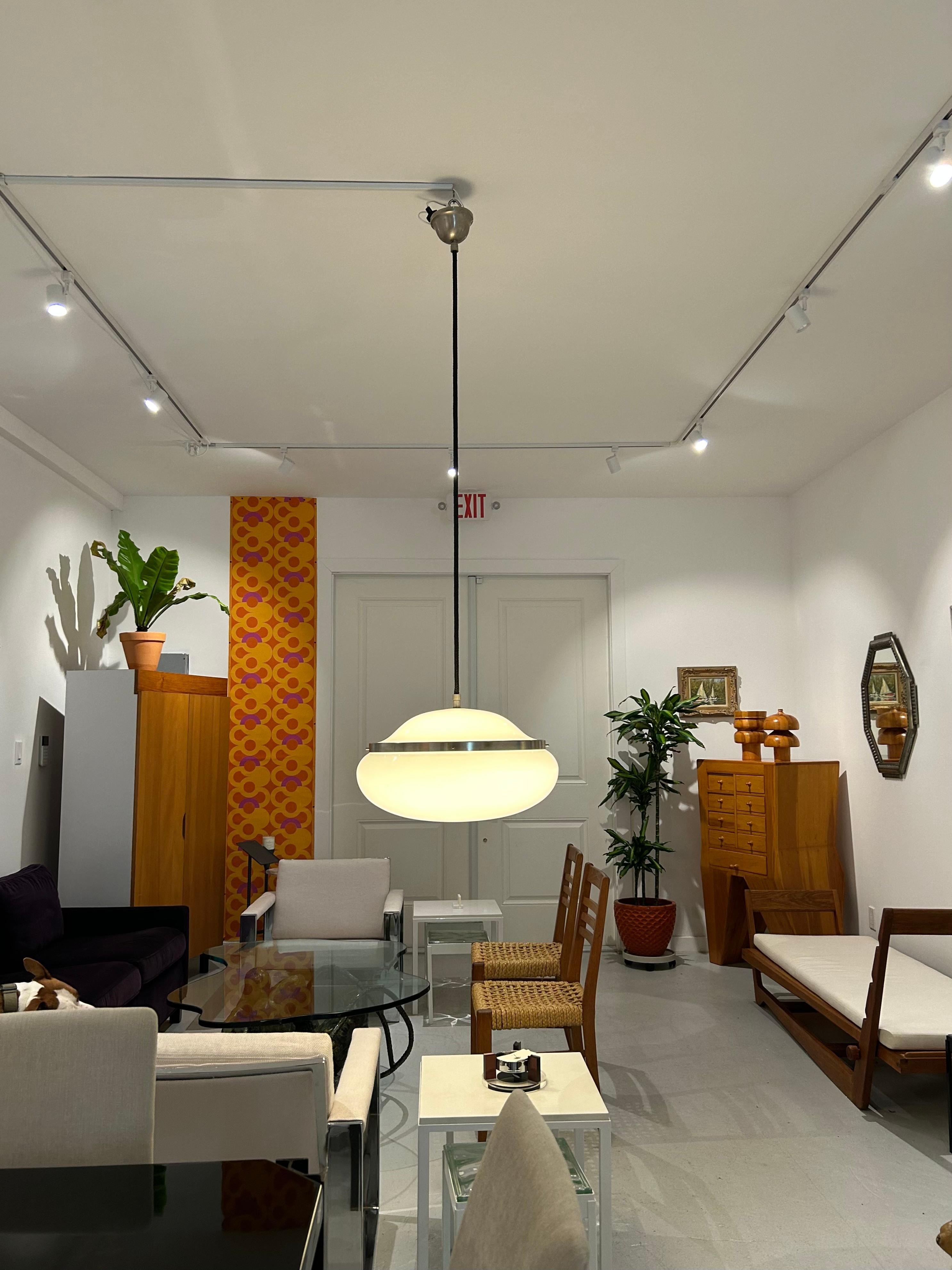 Lampada a sospensione a soffitto disegnata nel 1959 da Gianemilio Piero e Ana Montis e prodotta da Kartell negli anni '60, ha un paralume in plastica bianca opaca composto da due metà che sono collegate dalla fascia centrale in ottone nichelato e da