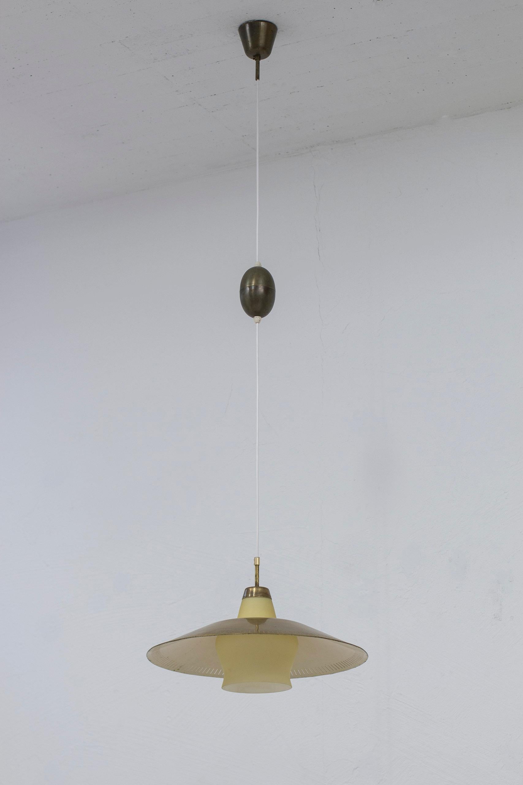 Ceiling pendant light designed by Harald Notini. Produced in Stockholm, Sweden by Arvid Böhlmarks lampfabrik during the 1940s. Light yellow opal glass with large brass shade. Brass extension 