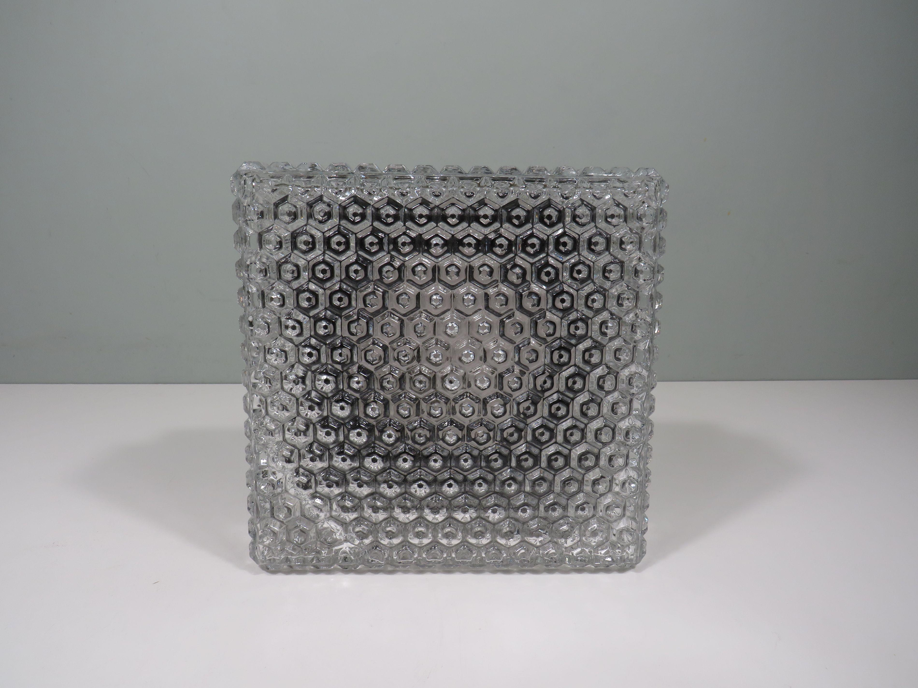 Optez pour une qualité authentique avec l'applique ou le plafonnier Nikos ! Le verre en forme de cube avec un relief structuré donne un aspect raffiné et permet une distribution douce de la lumière. La plaque murale est en bakélite noire, un