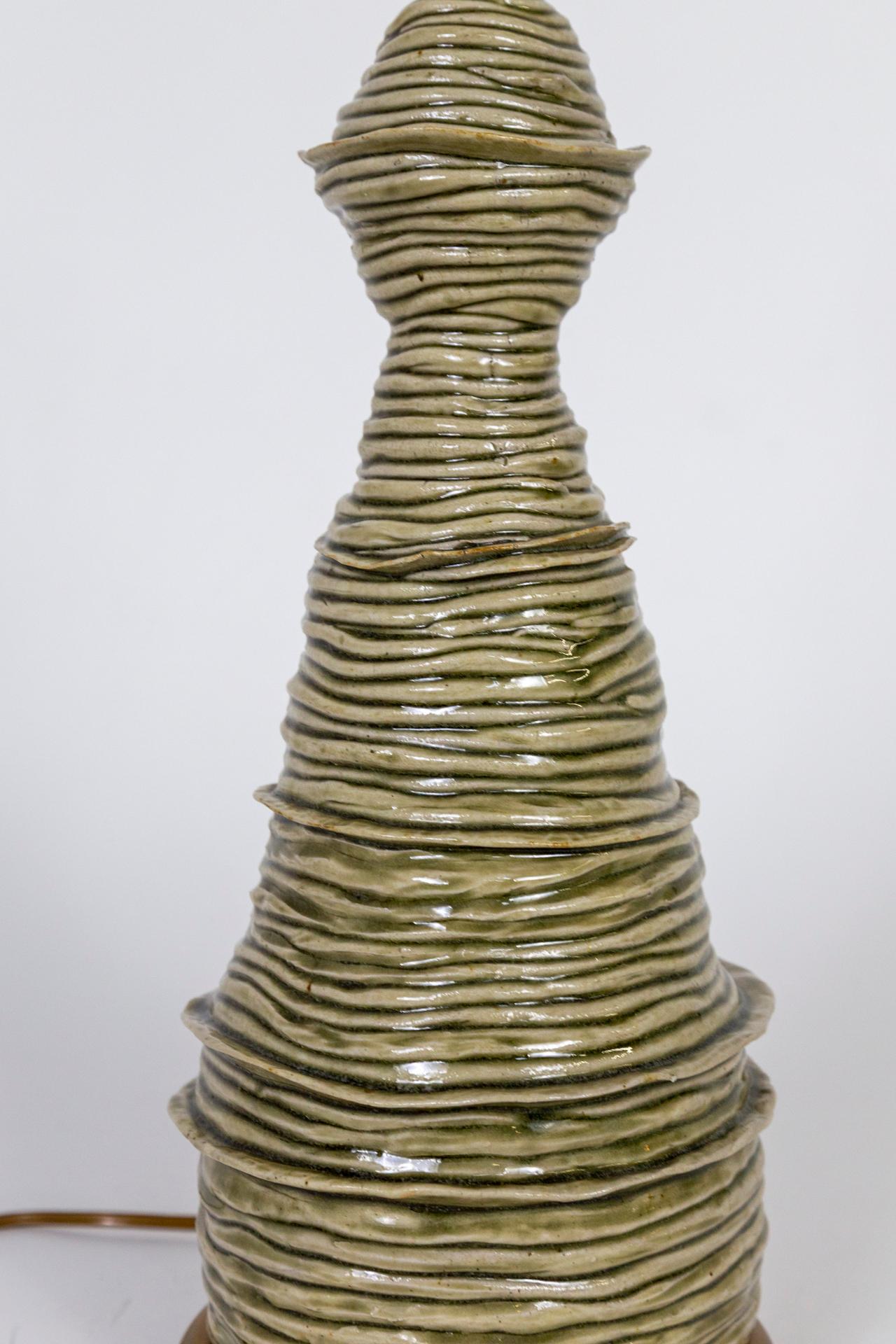 A unique, hand-made ceramic lamp made of slender coils wrapped into a whimsical, organic, tower shape; glazed in muted olive-celadon color. Newly restored with a weighted, brass base in a complimentary shape. Wired with a dimmer switch on the