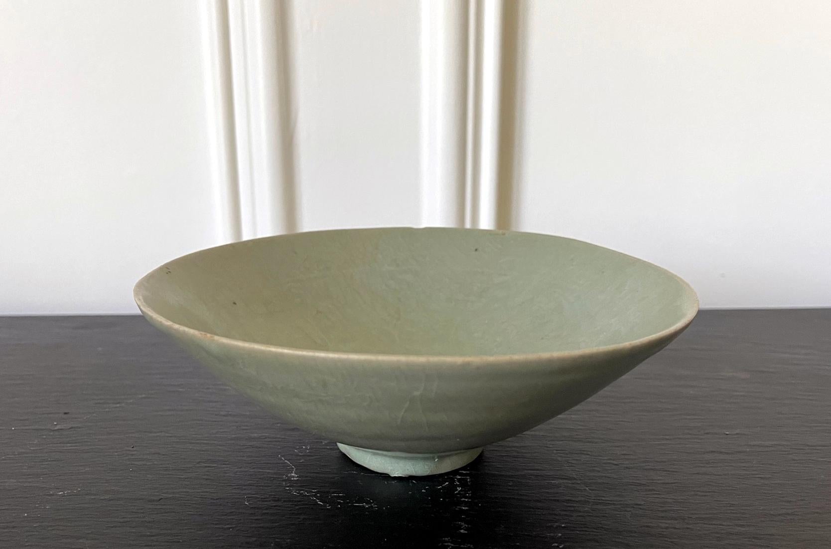 An antique Korean ceramic tea bowl with celadon glaze from Goryeo dynasty, circa 12th century. The thin-walled stoneware bowl was potted delicately with a subtle irregularity in shape. Of an elegant conical form, the bowl rises on a small ring base