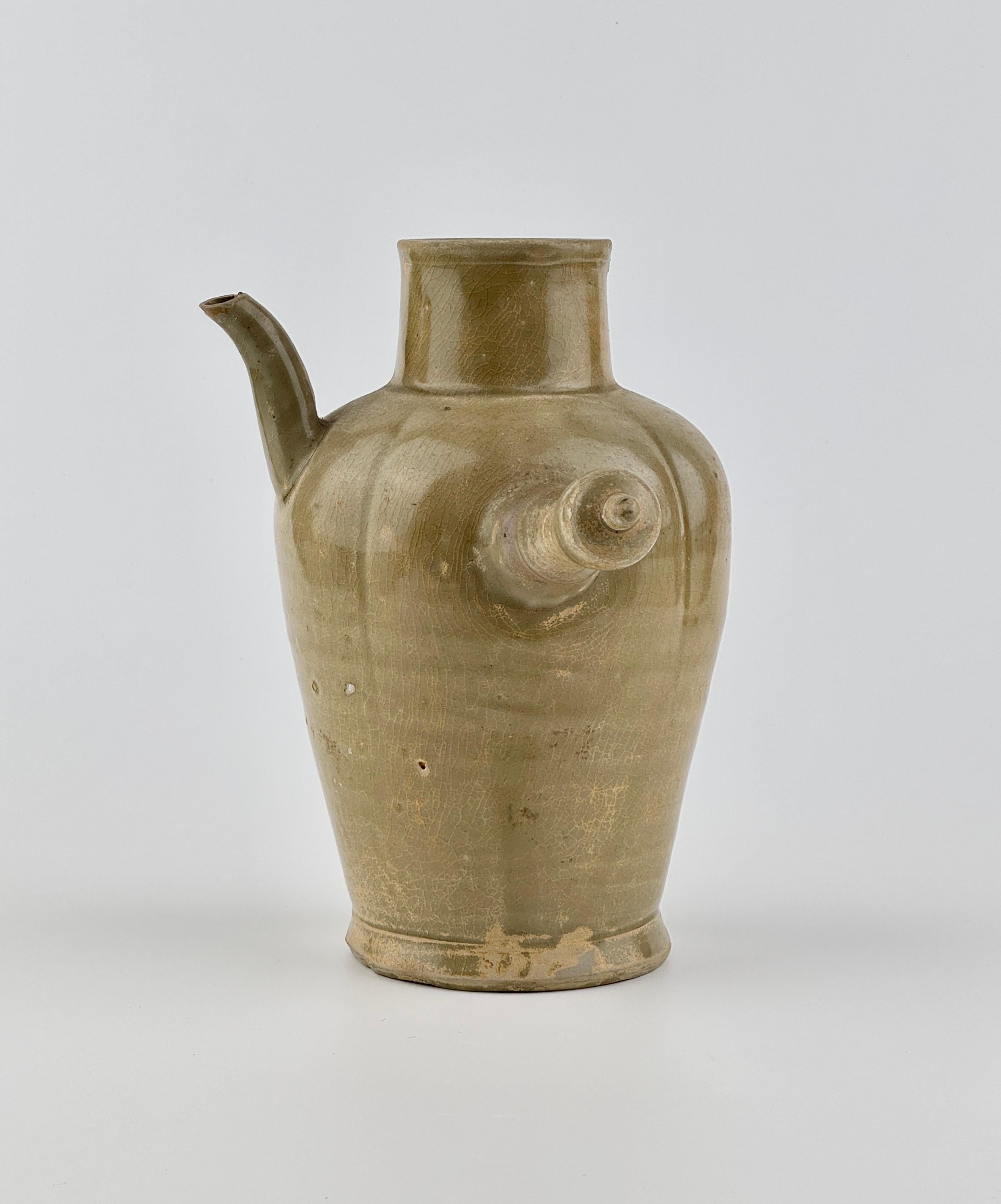 Celadon-glazed ewer characterized by its simple and functional design. The piece features a straight handle extending horizontally from the body and a short spout for pouring liquids. Its surface is coated with a soft, olive-green glaze, which is