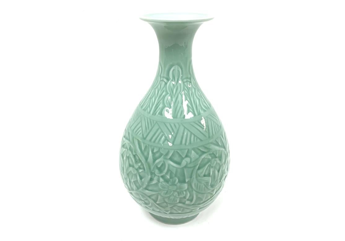Un vase en celedon caractérisé par sa glaçure vert jade distinctive et sa décoration sculptée complexe.  Les motifs floraux torsadés, les motifs géométriques et les méandres chinois estampés ou sculptés visibles sur le corps sont un élément