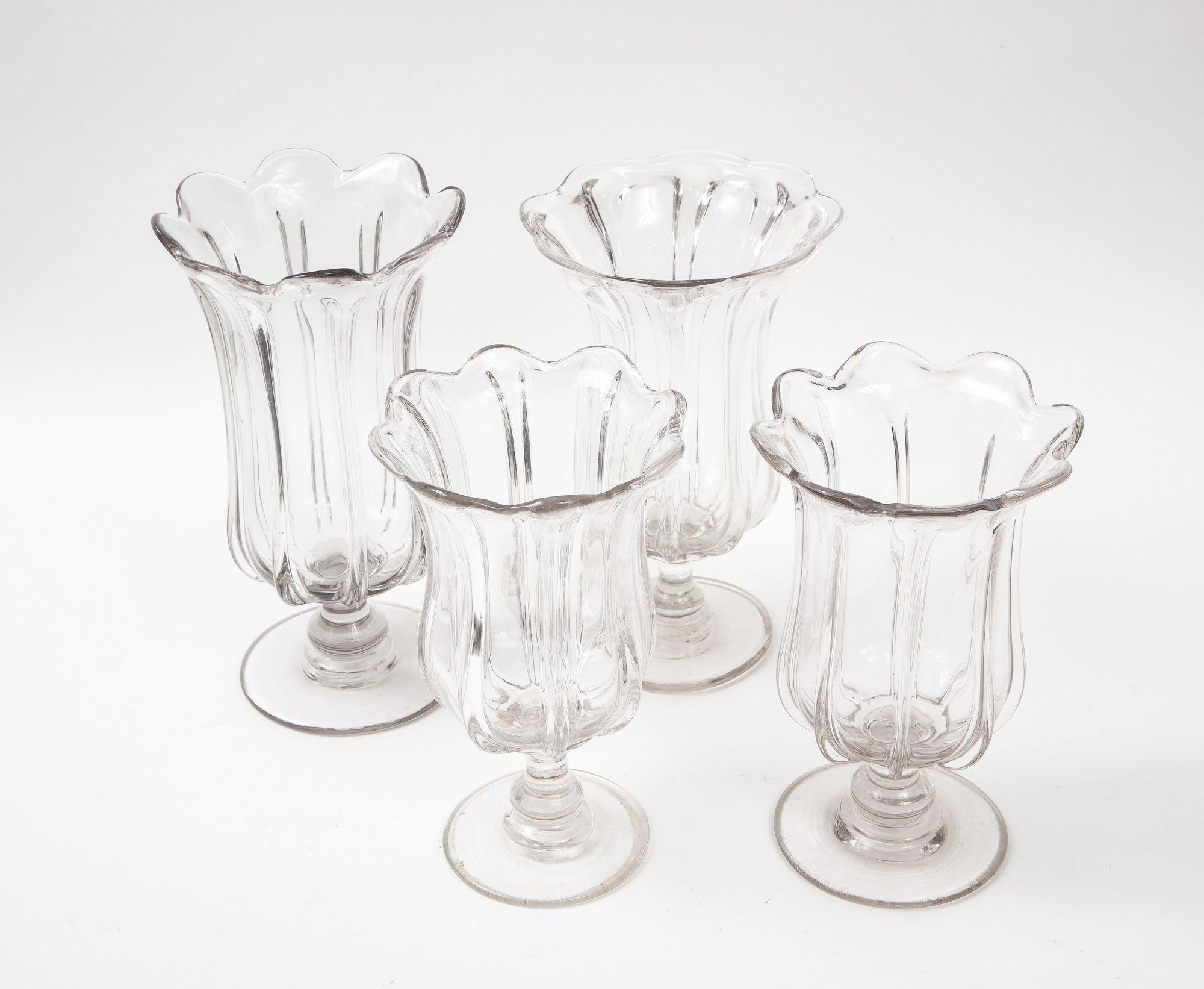 A collection of four heavy clear leaded glass footed vases of shaped and ribbed form with flared scalloped rims, known as celery vases. Elegant table or shelf decoration with or without flowers/celery. England, 19th century.