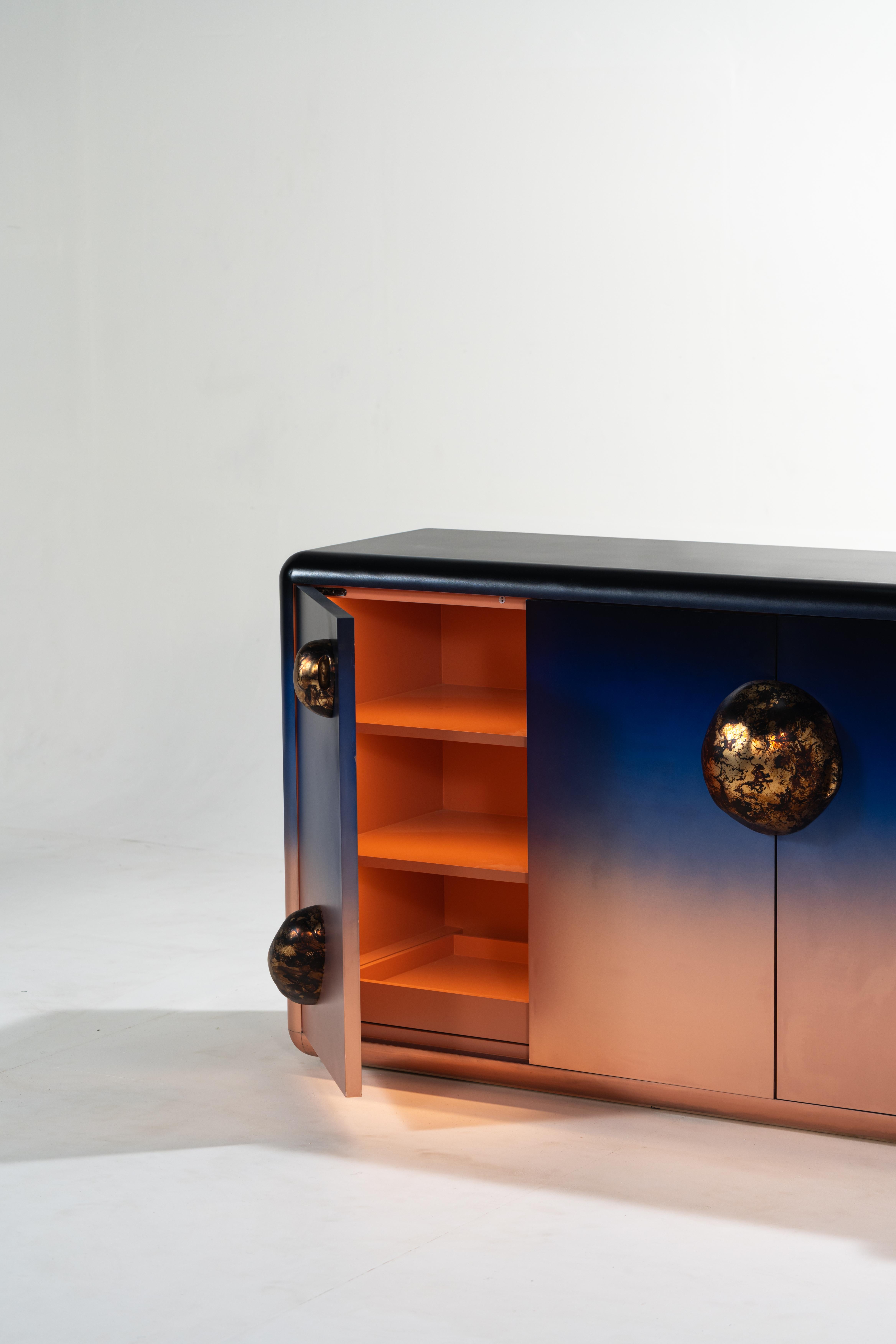 Celestial forms on the extravagant Celestial Console against coppery blue skies. A fabulous cabinet for your home which appears to be a sculptural piece but is a functional piece of furniture. 
An ethereal cabinet covered in copper with the gradient