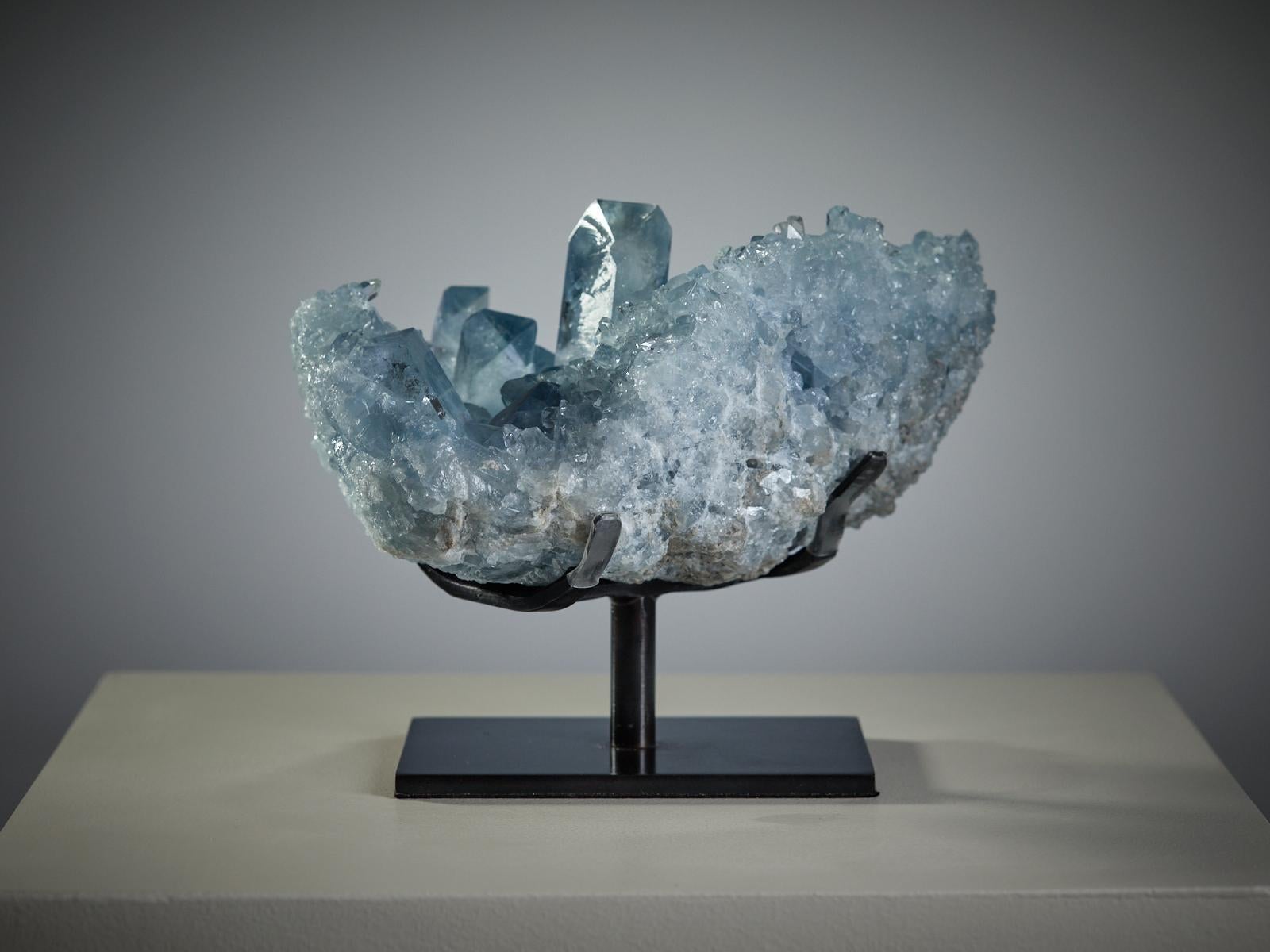Eine faszinierende Celestit-Geode aus Sakoany, Majunga, Madagaskar, mit Kristallen in verschiedenen Größen in einer anmutigen, natürlichen Komposition. In der Mitte erhebt sich ein markanter, wohlgeformter Kristall, der von einer zarten Ansammlung