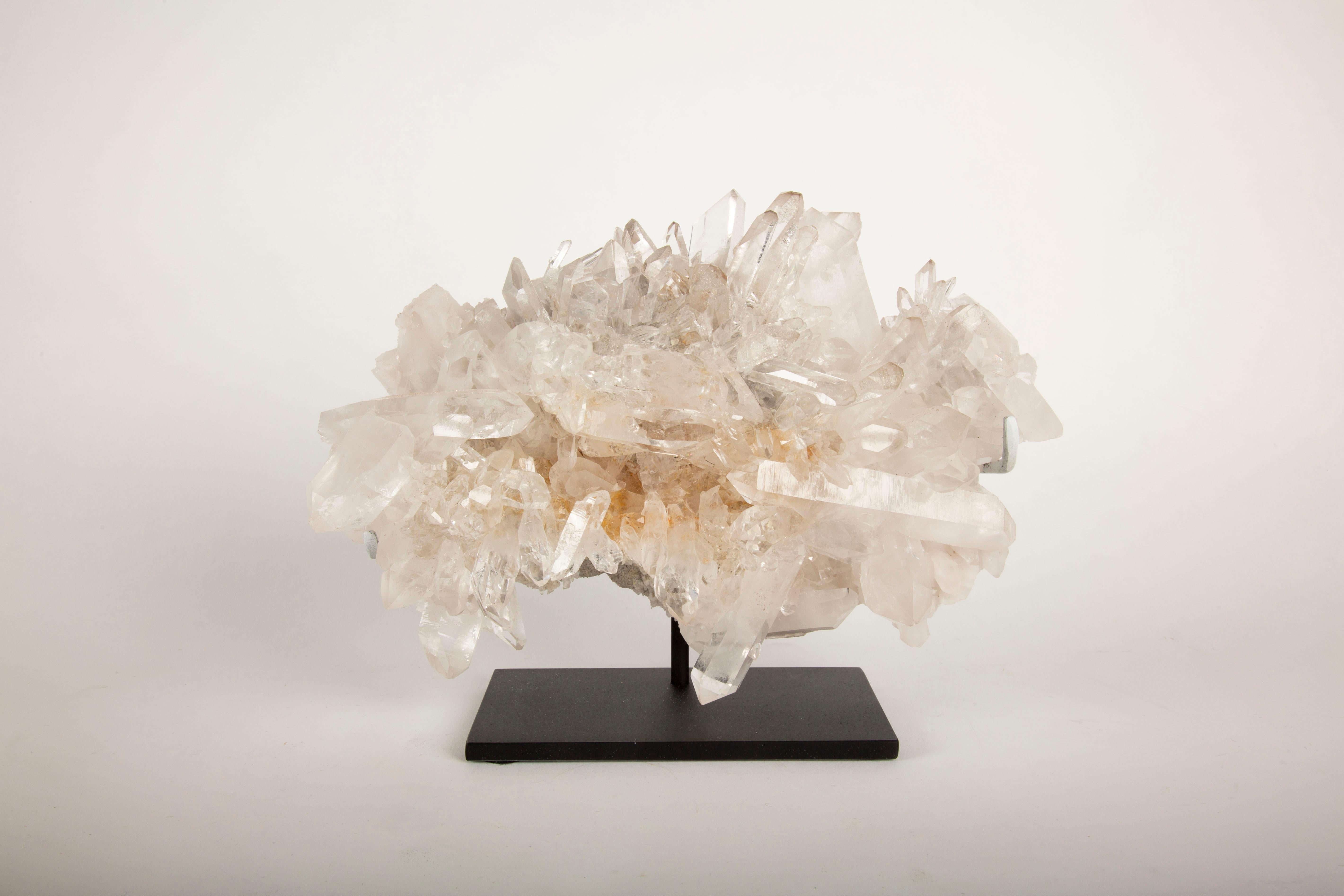 This stunning rock crystal cluster, custom mounted on a sleek black base, showcases the natural beauty of Arkansas-mined crystals. The piece features an impressive array of clear and translucent crystal formations, with sharp, well-defined points