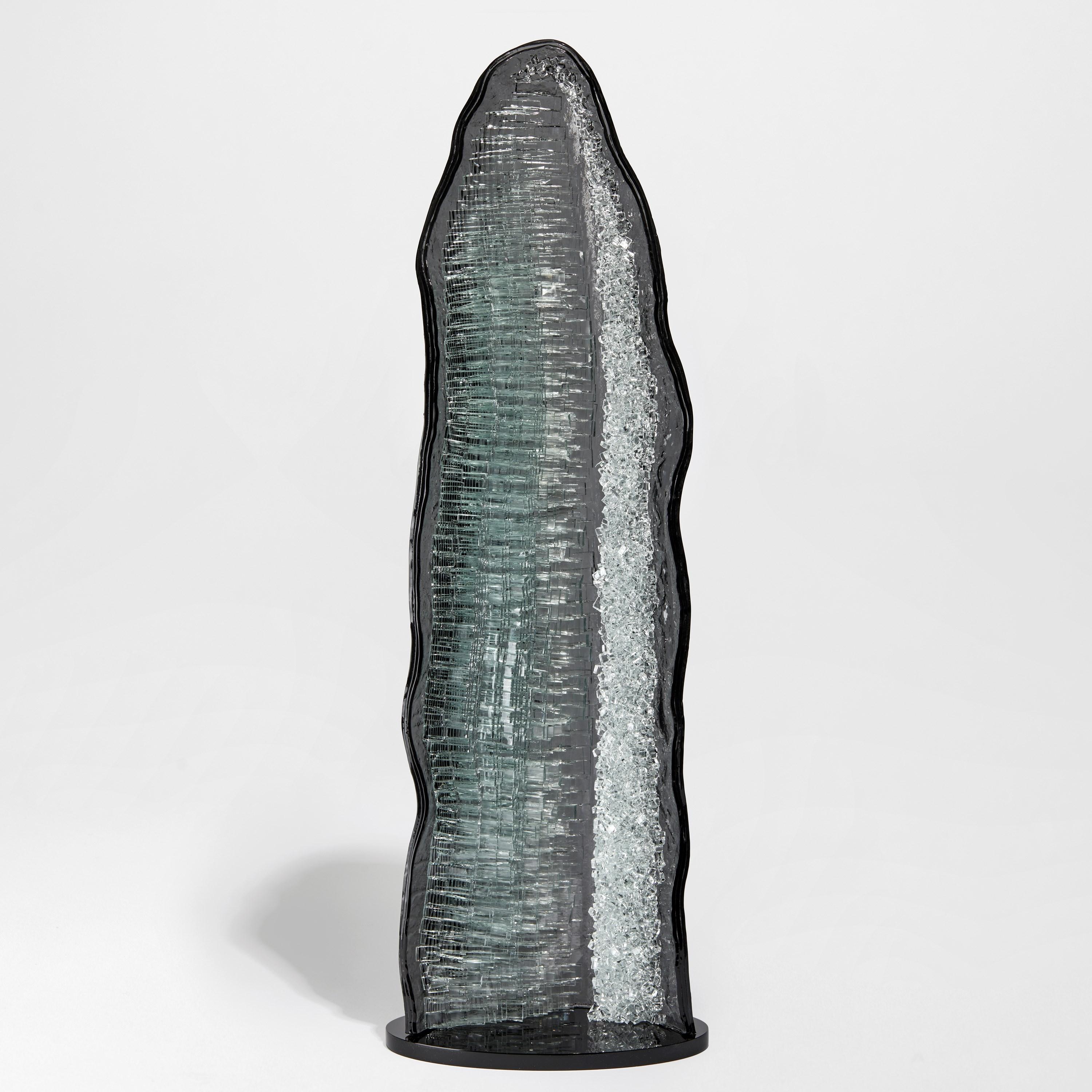 Celestite I ist eine einzigartige graue und klare Glasskulptur des britischen Künstlers Wayne Charmer. Inspiriert von dem Moment, in dem ein Gesteinsbrocken buchstäblich aufgesprengt wird, um einen Teppich aus funkelnden Edelsteinen freizulegen, hat