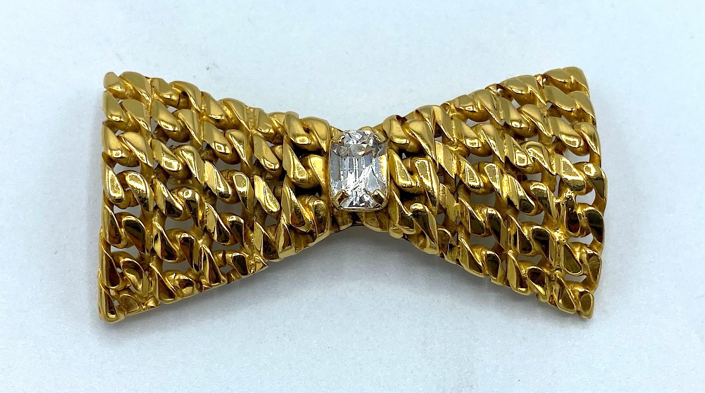 A charming bow brooch by Celine from the 1990s. Twelve rows from long to short of curb link chain are soldered together to create the bow shape. The center is mounted with a single emerald cut rhinestone. The brooch measures 2 inches wide, 1.13