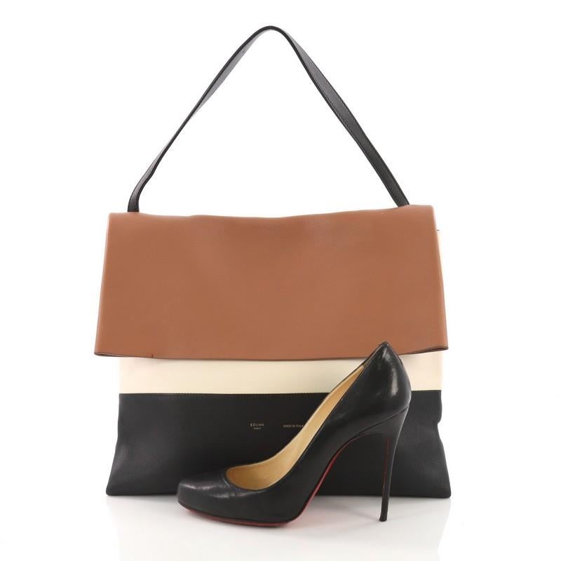 This Celine All Soft Tote Leather, crafted from brown and black leather, features a flat leather shoulder strap, subtle stamped Celine logo, and silver-tone hardware. Its flap opens to a brown suede interior. **Note: Shoe photographed is used as a