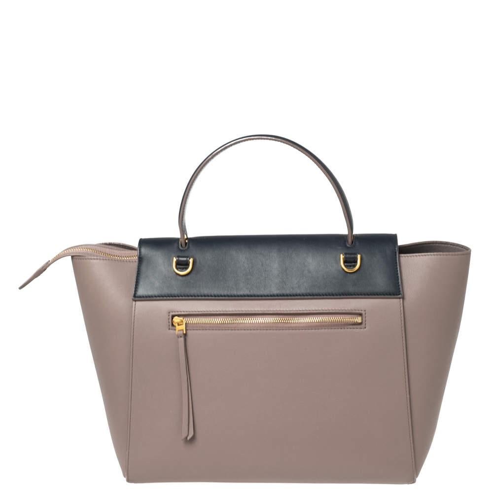 Bags from Celine are symbols of excellent craftsmanship and timeless design. This beige/navy blue creation has been crafted from leather and styled with a front tuck-in flap and knotted belt details. It flaunts a single top handle and a well-spaced