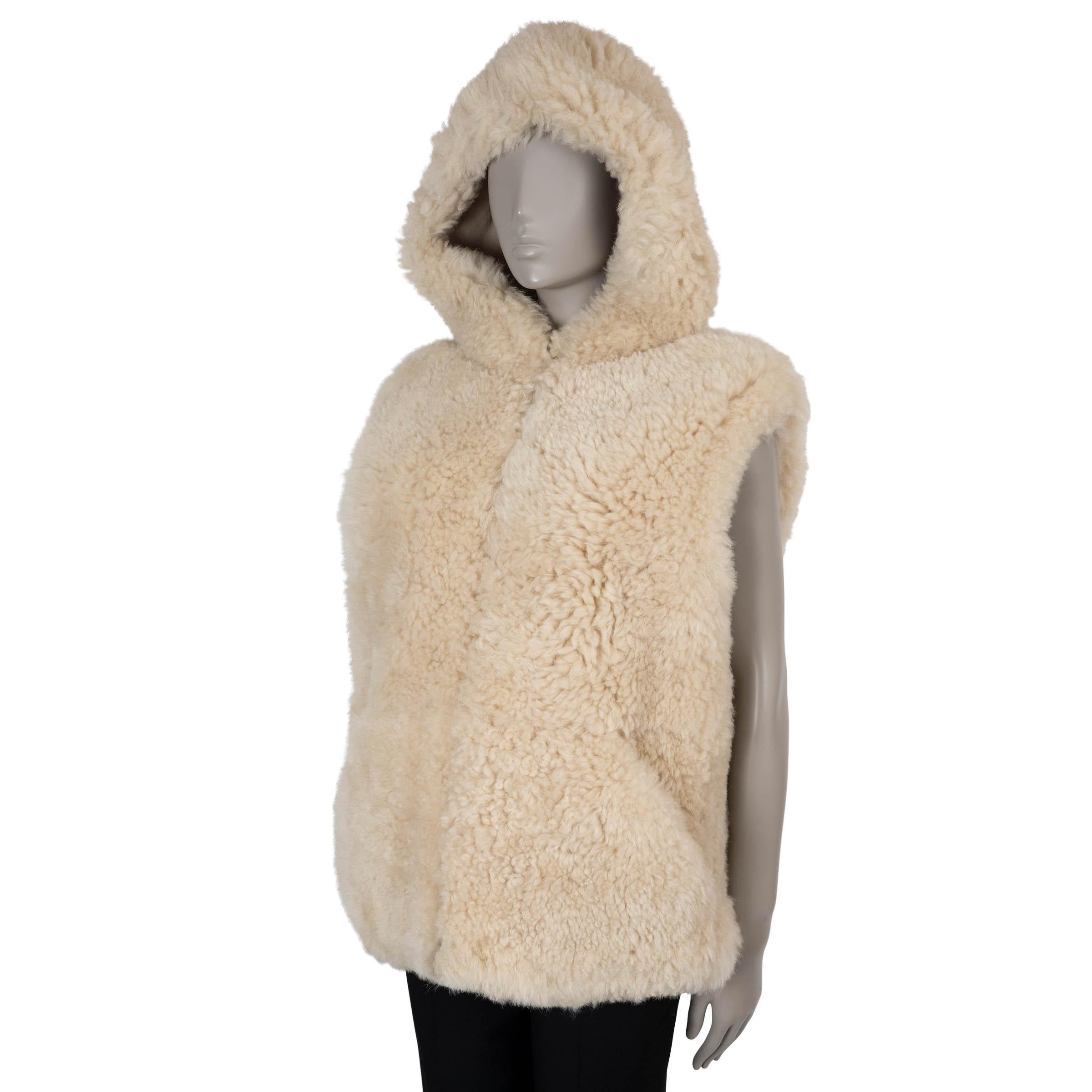 Este chaleco 100% auténtico de Celine está confeccionado en shearling beige y diseñado en una silueta de corte recto con una longitud corta y una acogedora capucha. Presenta dos bolsillos delanteros y se abre con una cremallera oculta para un