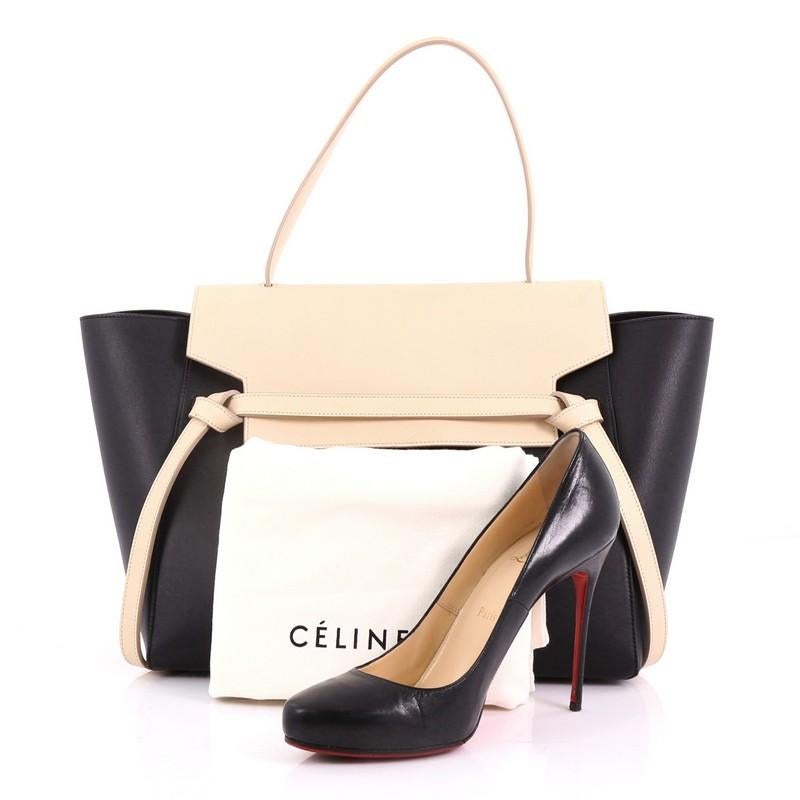 This Celine Belt Bag Calfskin Small, crafted from black and white calfskin leather, features expanded wings, looped single top handle, back zip pocket, and gold-tone hardware. Its top zip closure opens to a black suede interior with slip pockets.