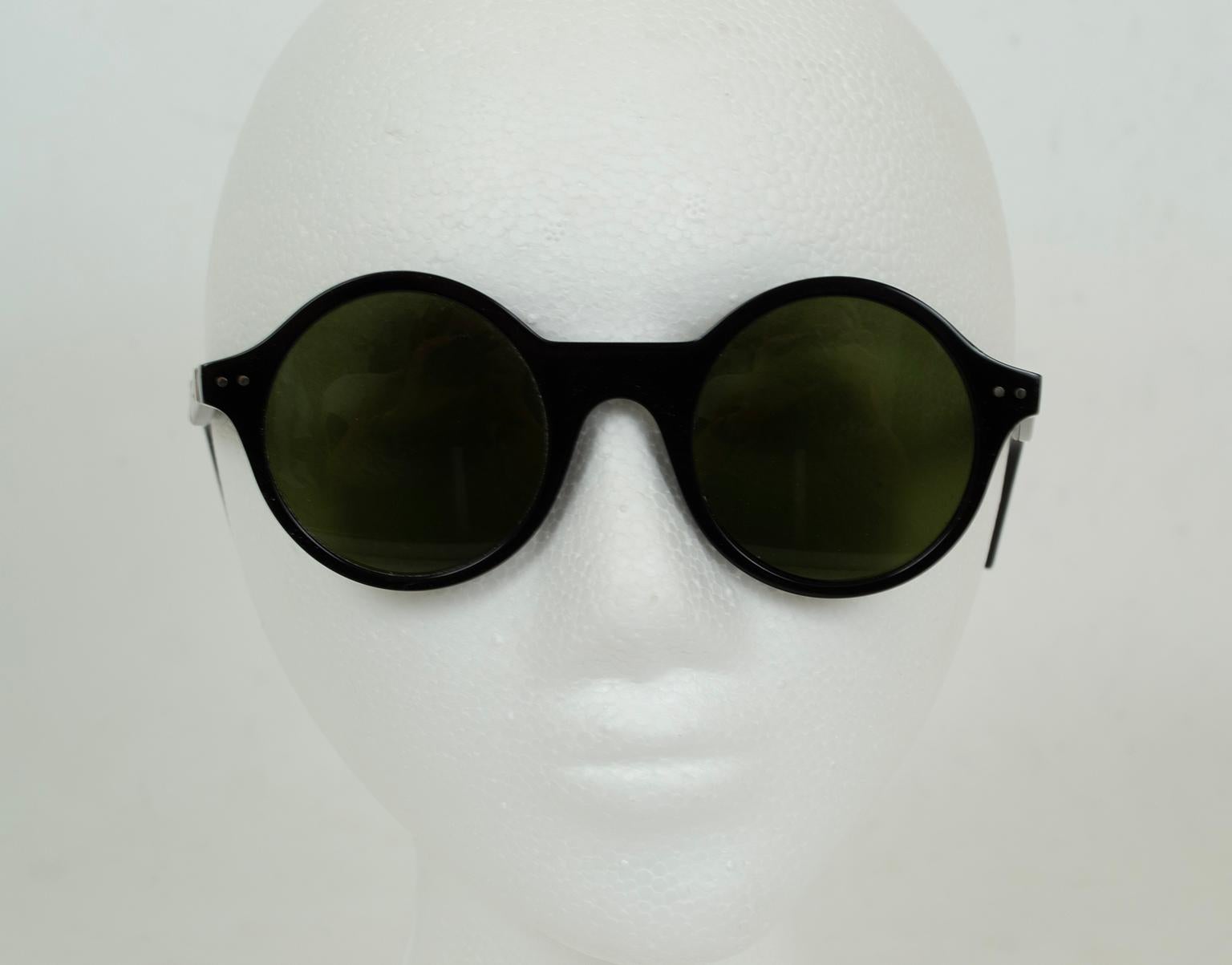 Lunettes de soleil aux verres parfaitement ronds, dotées d'un épais pont horizontal droit et de deux rivets argentés sur les branches ; verres UV gris-vert. Signature sur le bras gauche.

matériau : acétate
à noter : nettoyer avec un chiffon de
