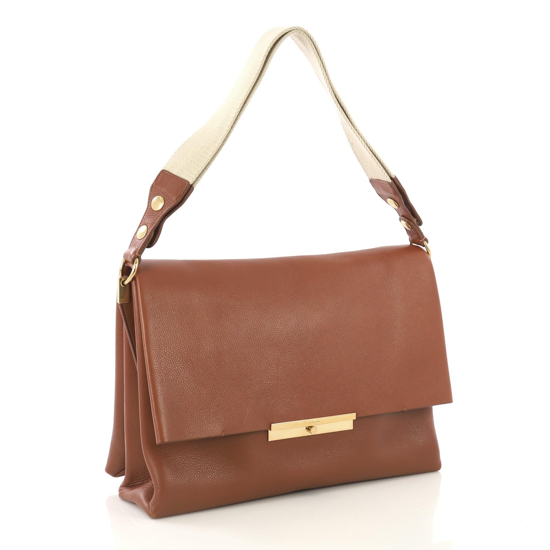This Celine Blade Shoulder Bag Leather, crafted in brown leather, features a flat canvas shoulder strap with button snaps that lengthen the strap and gold-tone hardware. The flap opens to a brown suede interior divided into two spacious open